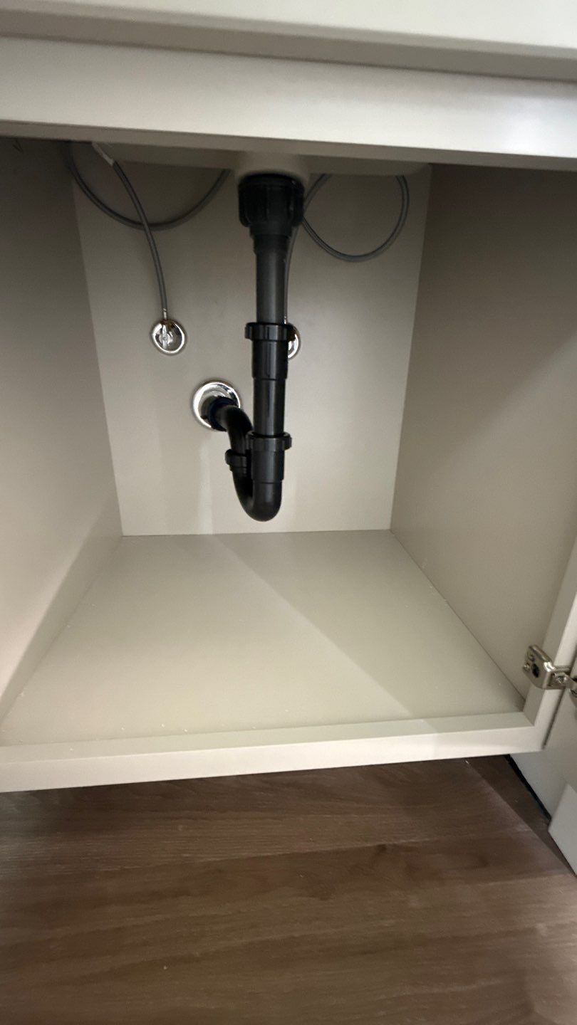 Open under-sink cabinet showing black drain pipes and plumbing on a white interior.