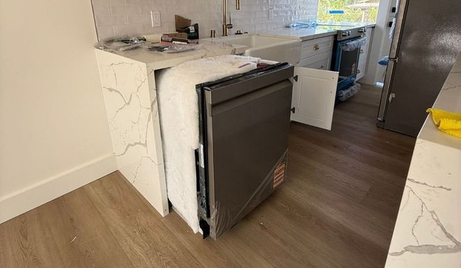 Kitchen with a built-in dishwasher open, showing a modern countertop and wood flooring.