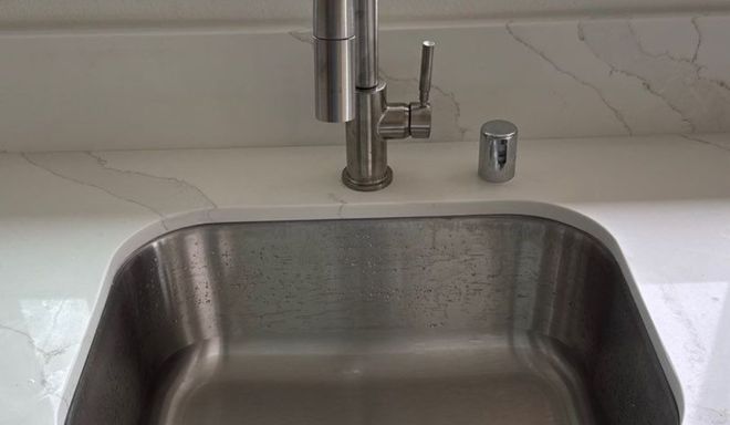 Stainless steel kitchen sink under a modern chrome faucet with a white countertop backsplash.