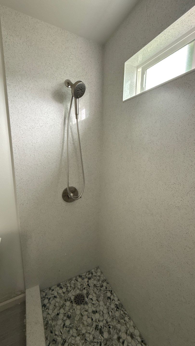 Small white shower stall with a handheld showerhead and a small frosted window.
