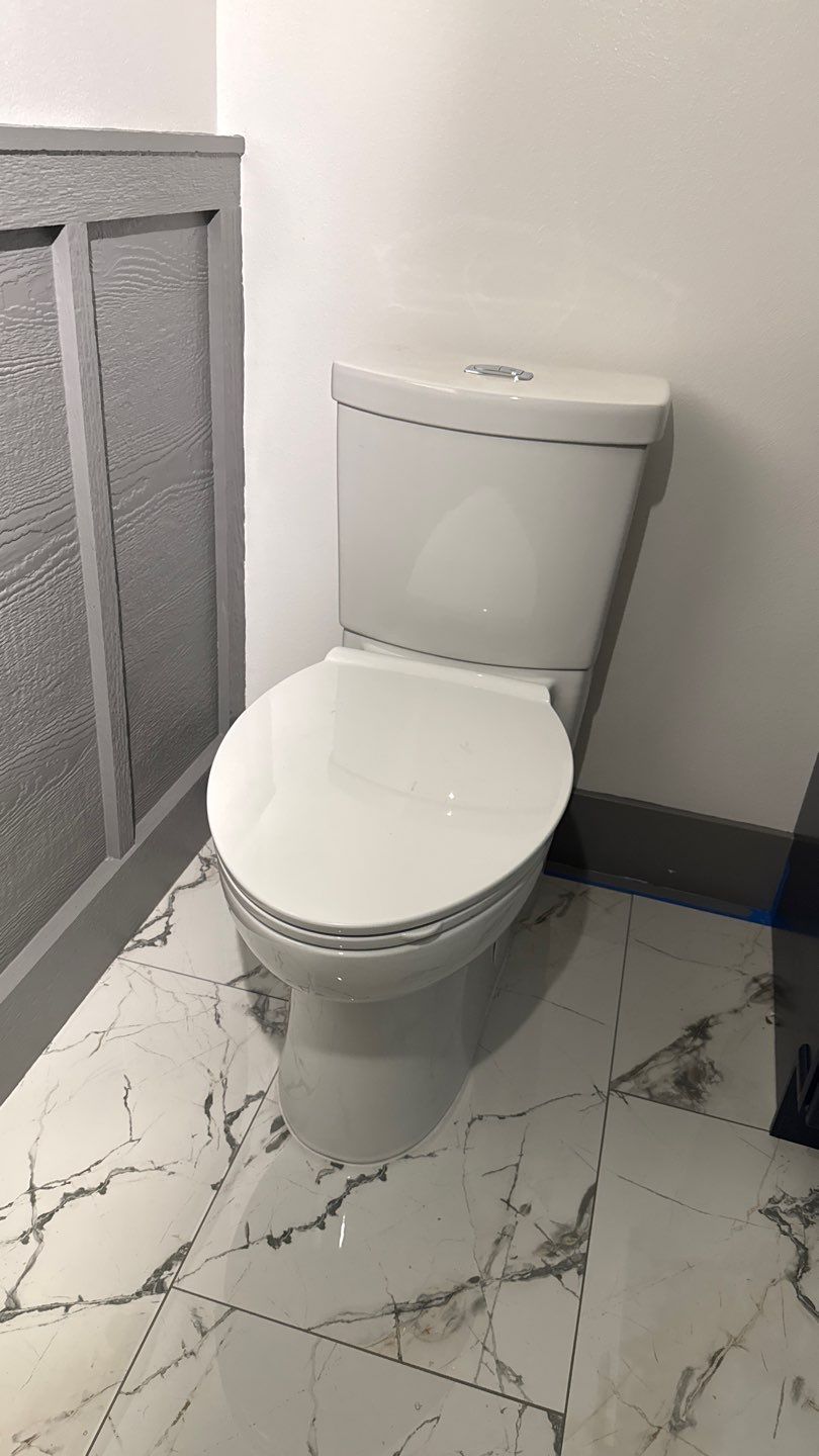 Small white toilet in a tiled bathroom beside a gray half wall.