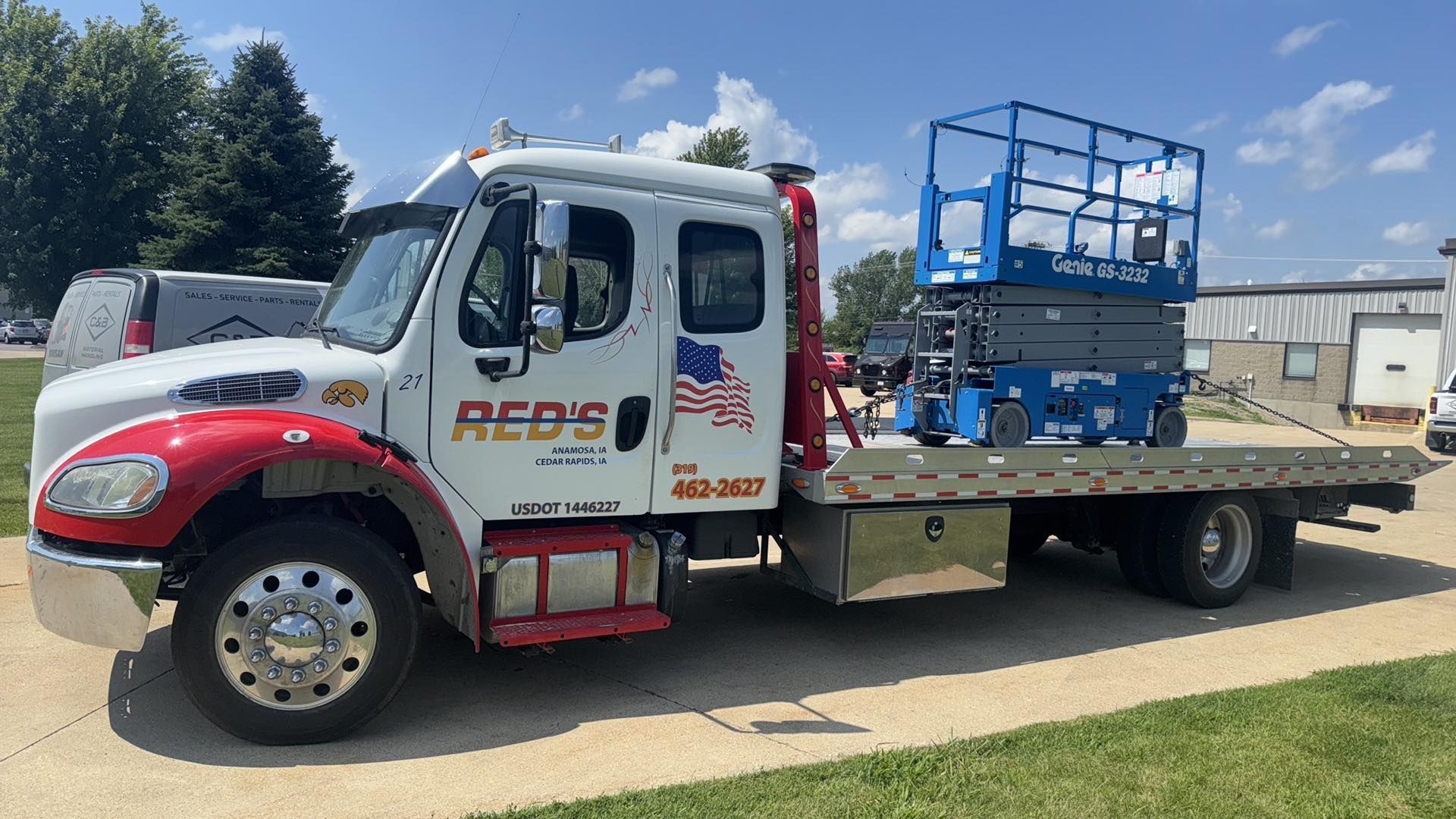 Flatbed truck with a blue scissor lift on the bed, parked outside with a blue sky.