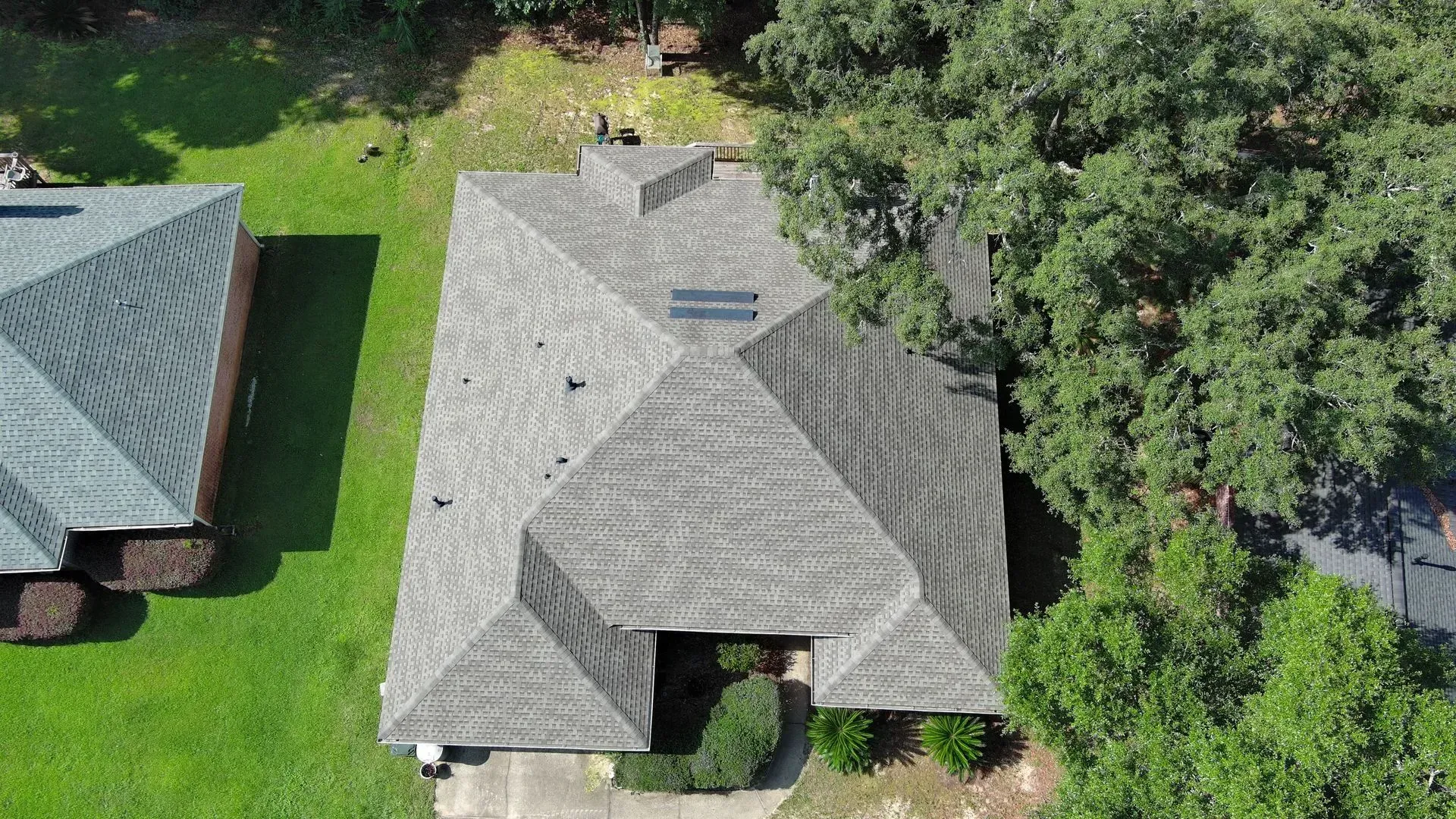 Overhead view of a house with a gray, multi-faceted roof surrounded by green grass and trees.