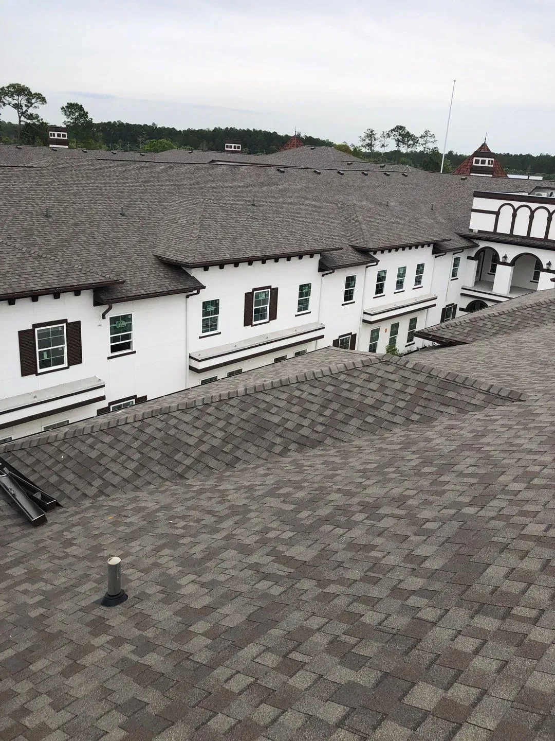 Building with brown roof shingles and white walls, topped with a gray cloudy sky.