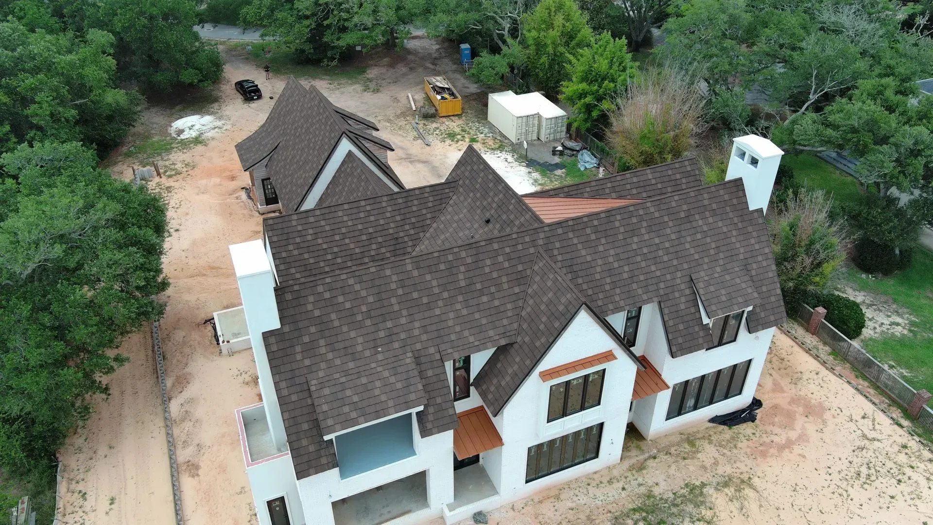 Aerial view of a white house with brown roof under construction, surrounded by trees and dirt.