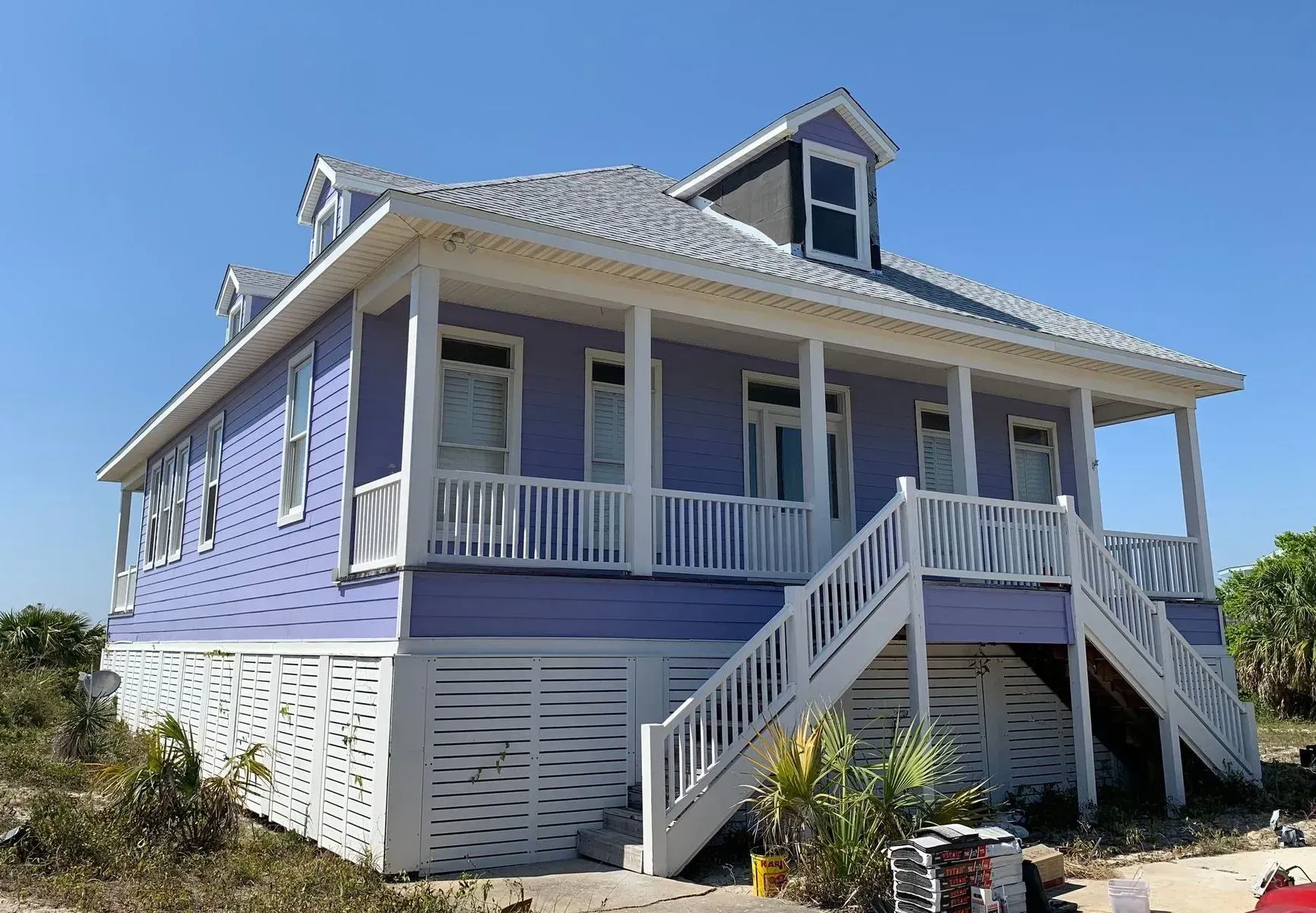 Purple two-story house with white trim, porch, and stairs against a clear blue sky.