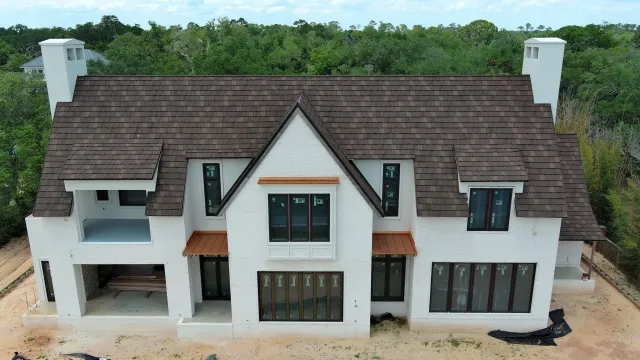Two-story white house with brown roof and black-framed windows, surrounded by trees.