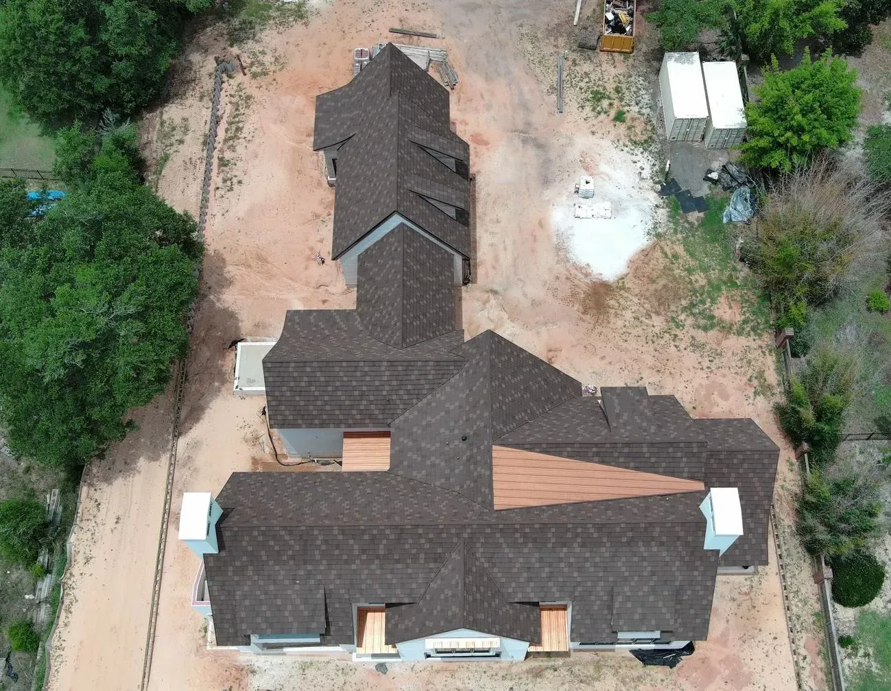 Overhead view of a house with a brown shingled roof, set on a construction site with dirt and green trees.