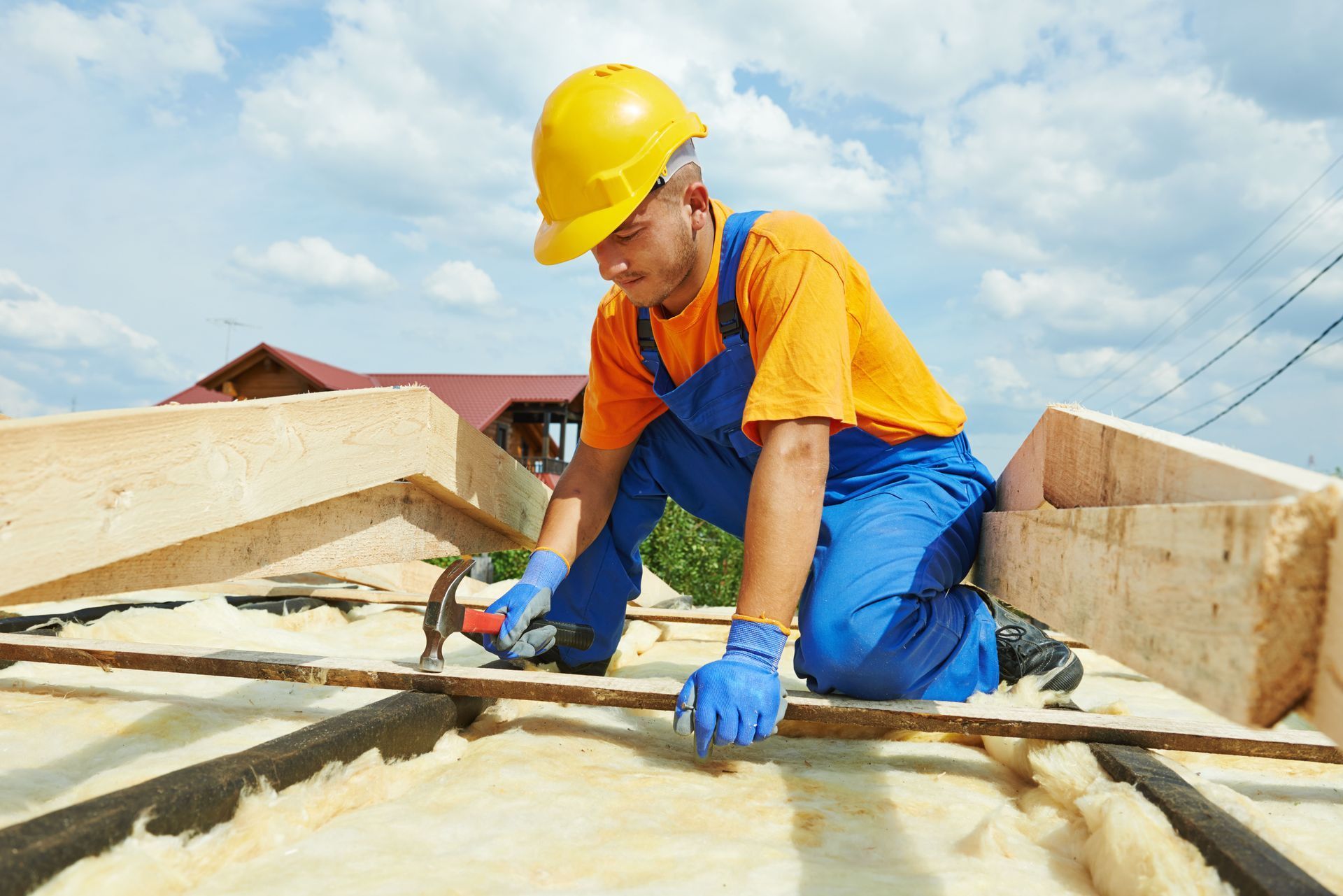 Roofer wearing a hard hat hammering on a roof under construction.