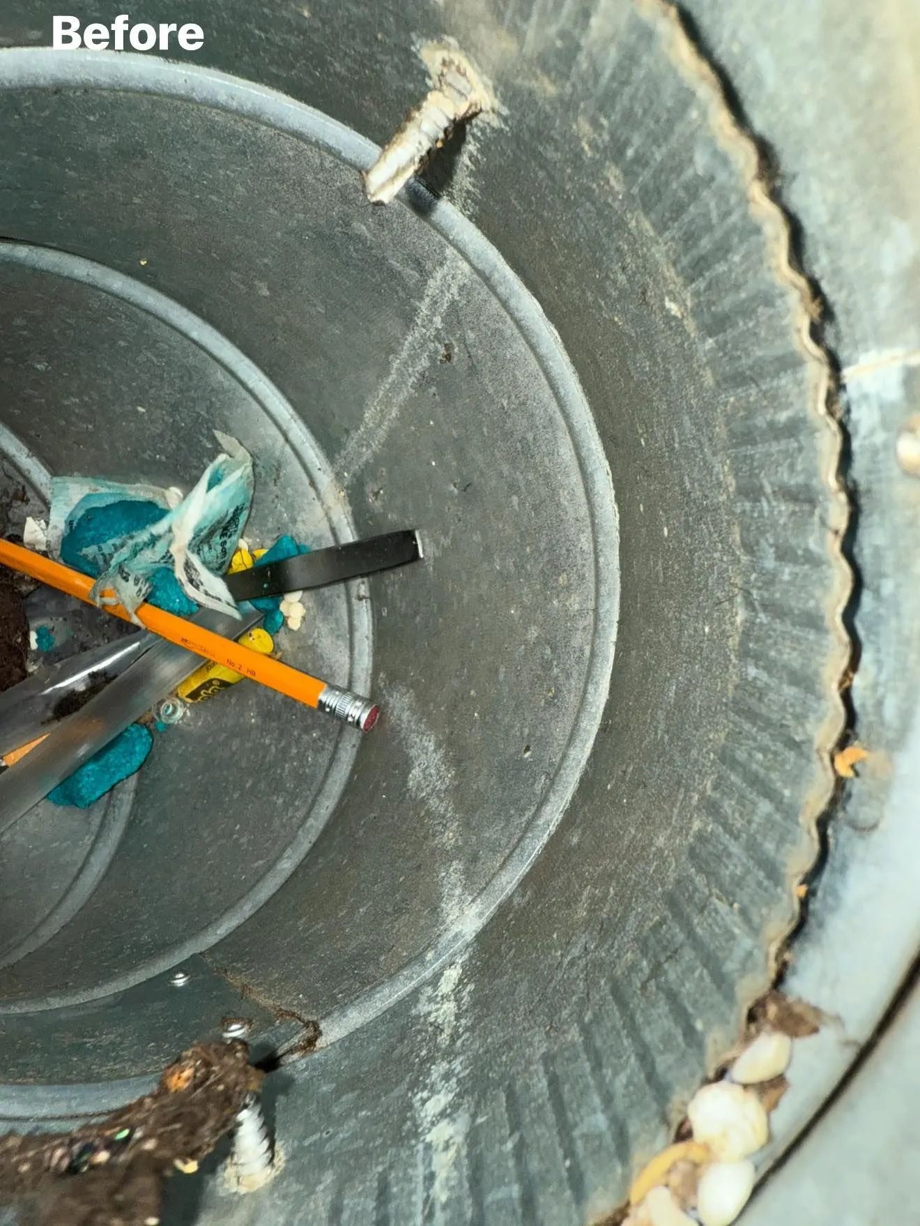 Inside of a dirty, cylindrical vent with debris like a pencil, plastic, and screws.