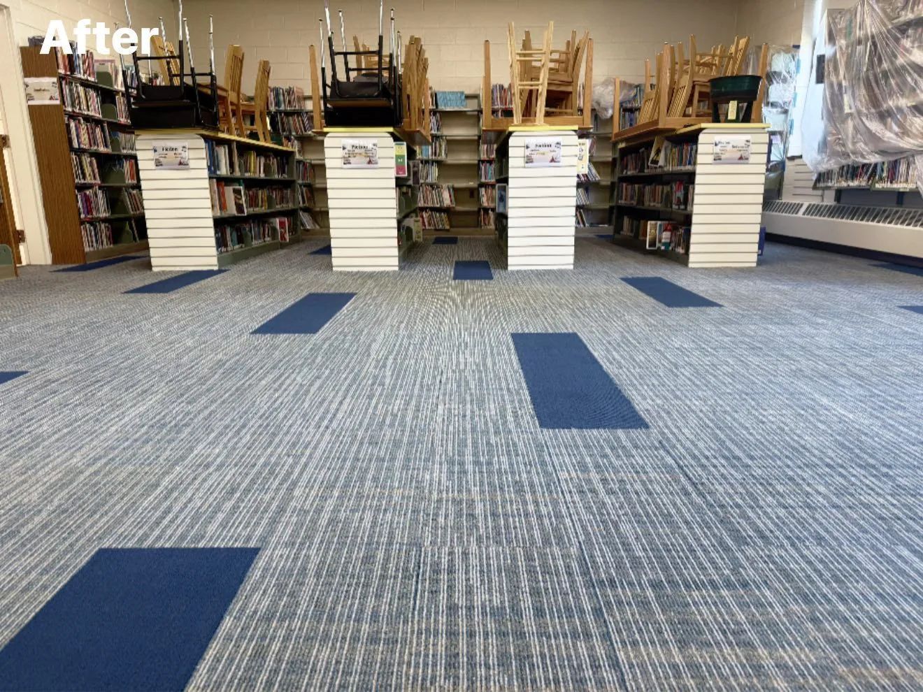 Library interior with blue and gray patterned carpet, bookshelves, and stacked chairs.