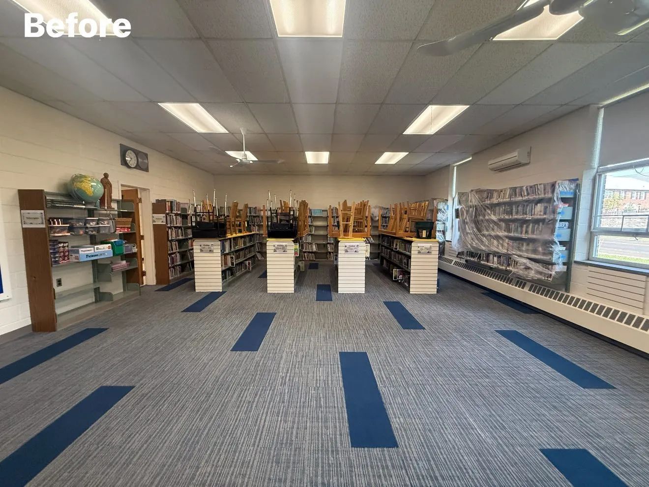 A library interior with bookshelves, a blue and gray carpet, and overhead lighting.