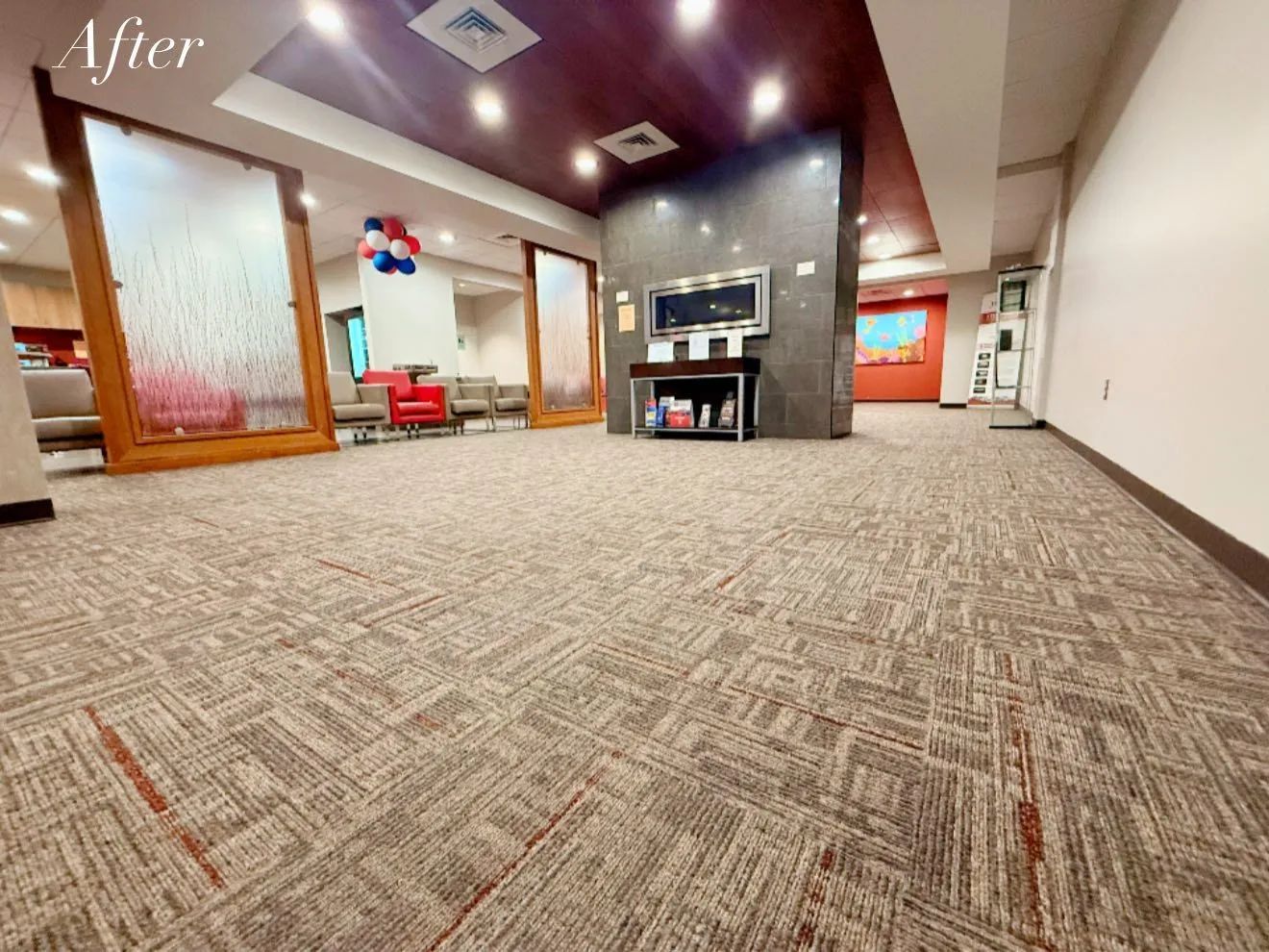 Lobby with patterned carpet, red ceiling accents, and a large central pillar with a TV and shelving unit.