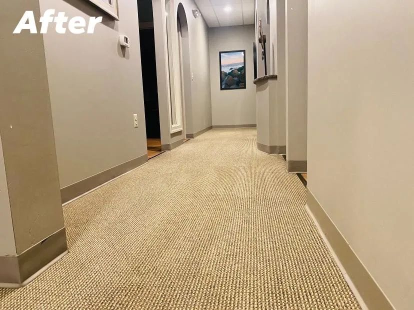 Long hallway with beige carpet, gray walls, and artwork. 