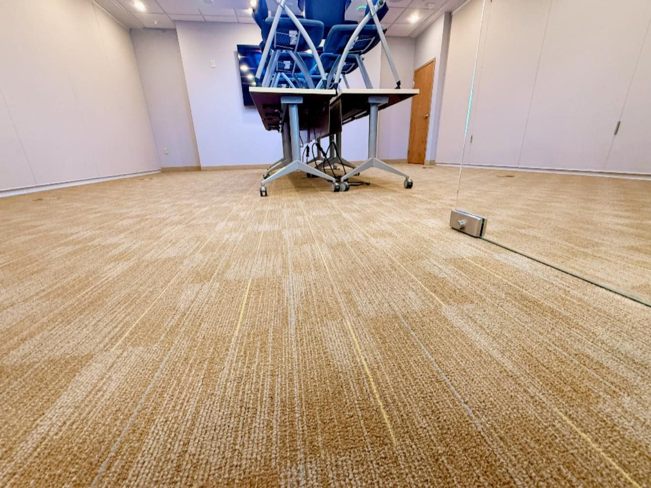 Room with tan carpet, tables, and chairs. A device sits on the floor with a wire.