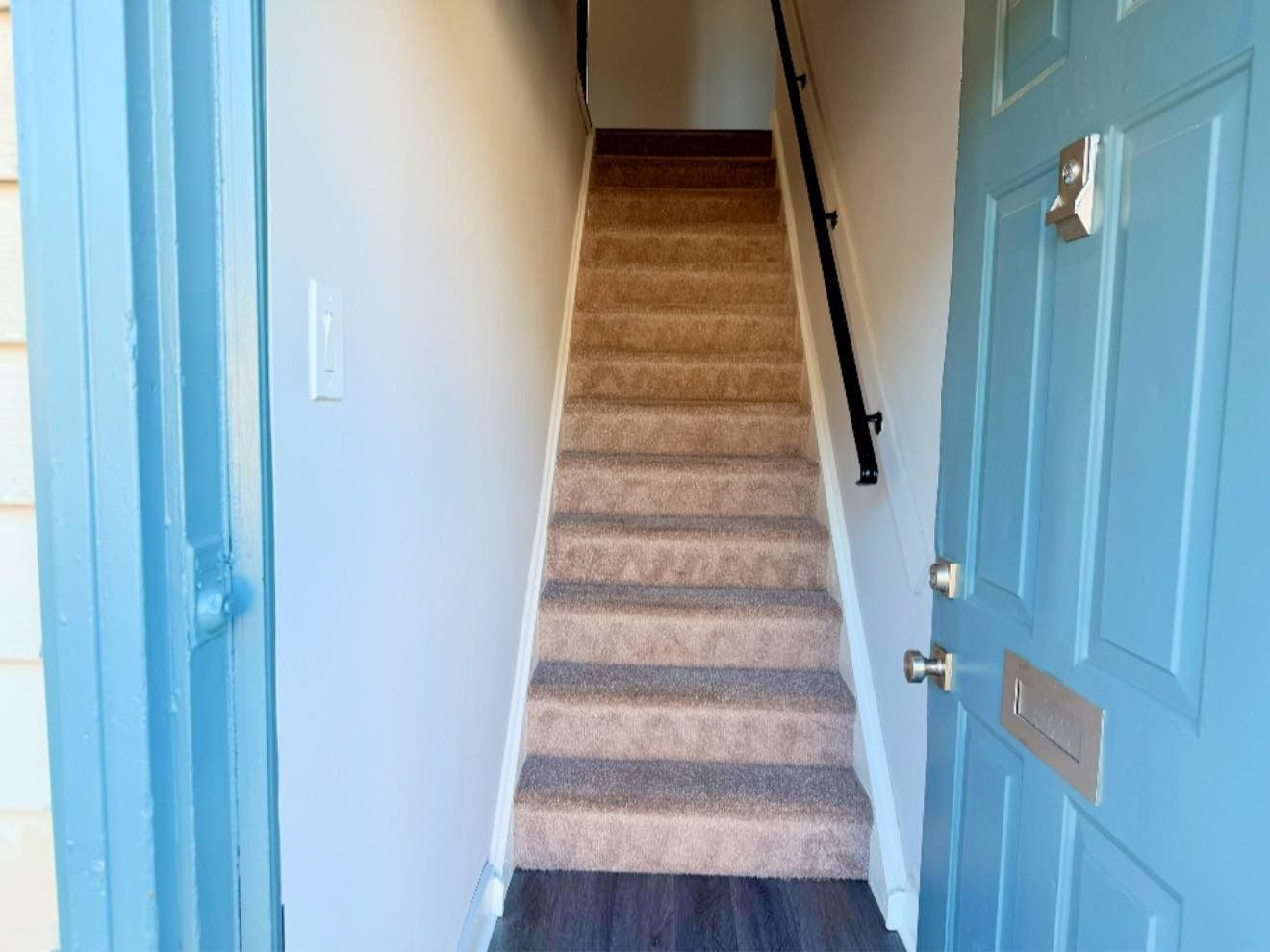 Open blue door leading into a narrow hallway with carpeted stairs.