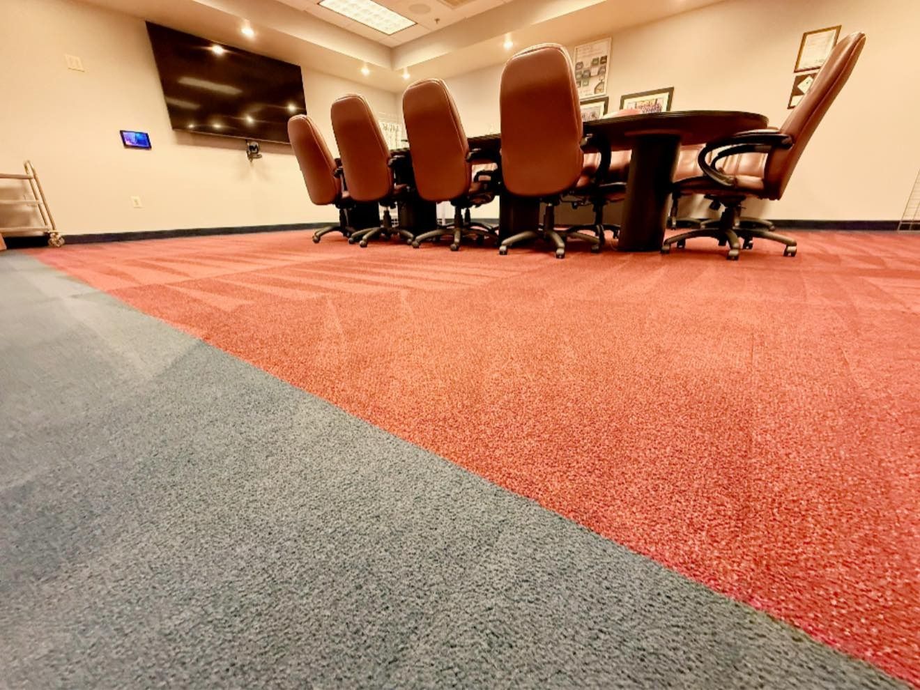 Conference room with red and gray carpet, round table, chairs, and a large screen on the wall.