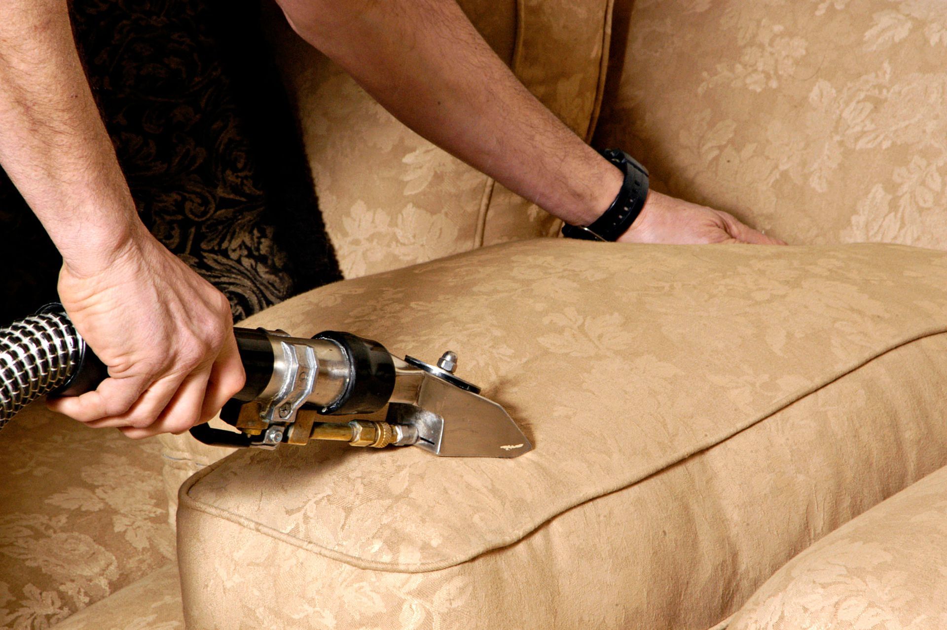 Person cleaning a beige couch cushion with an upholstery cleaning tool.