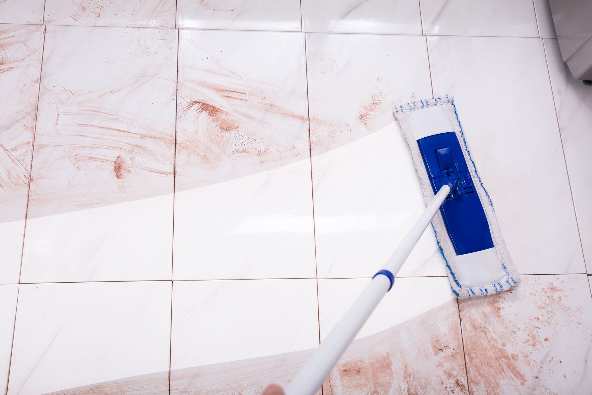 A person mopping a dirty, patterned tile floor with a blue and white mop.