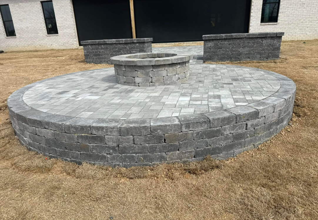A fire pit is sitting in the middle of a brick patio in front of a house.