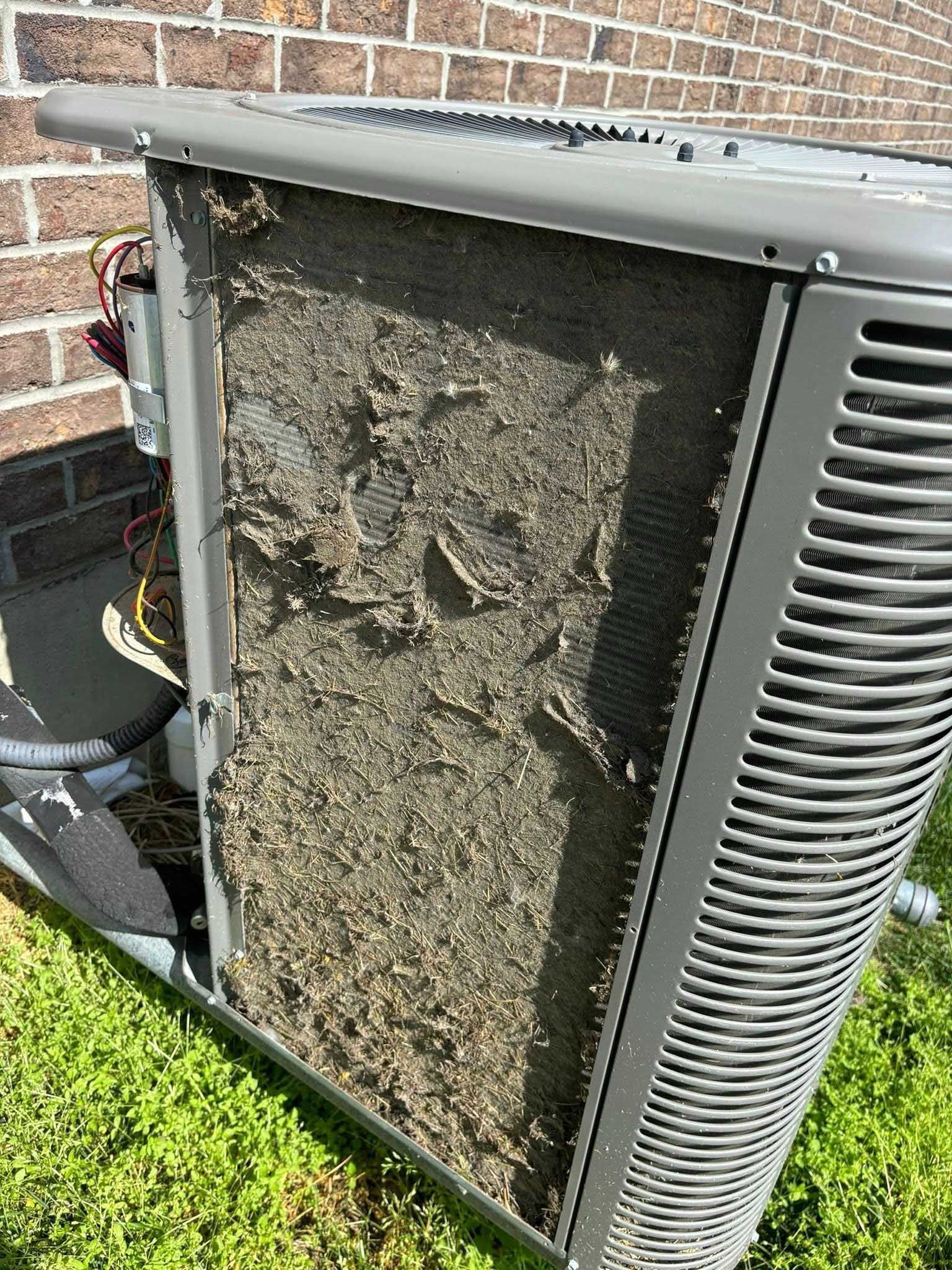 Air conditioner unit covered in debris next to a brick wall and grass.
