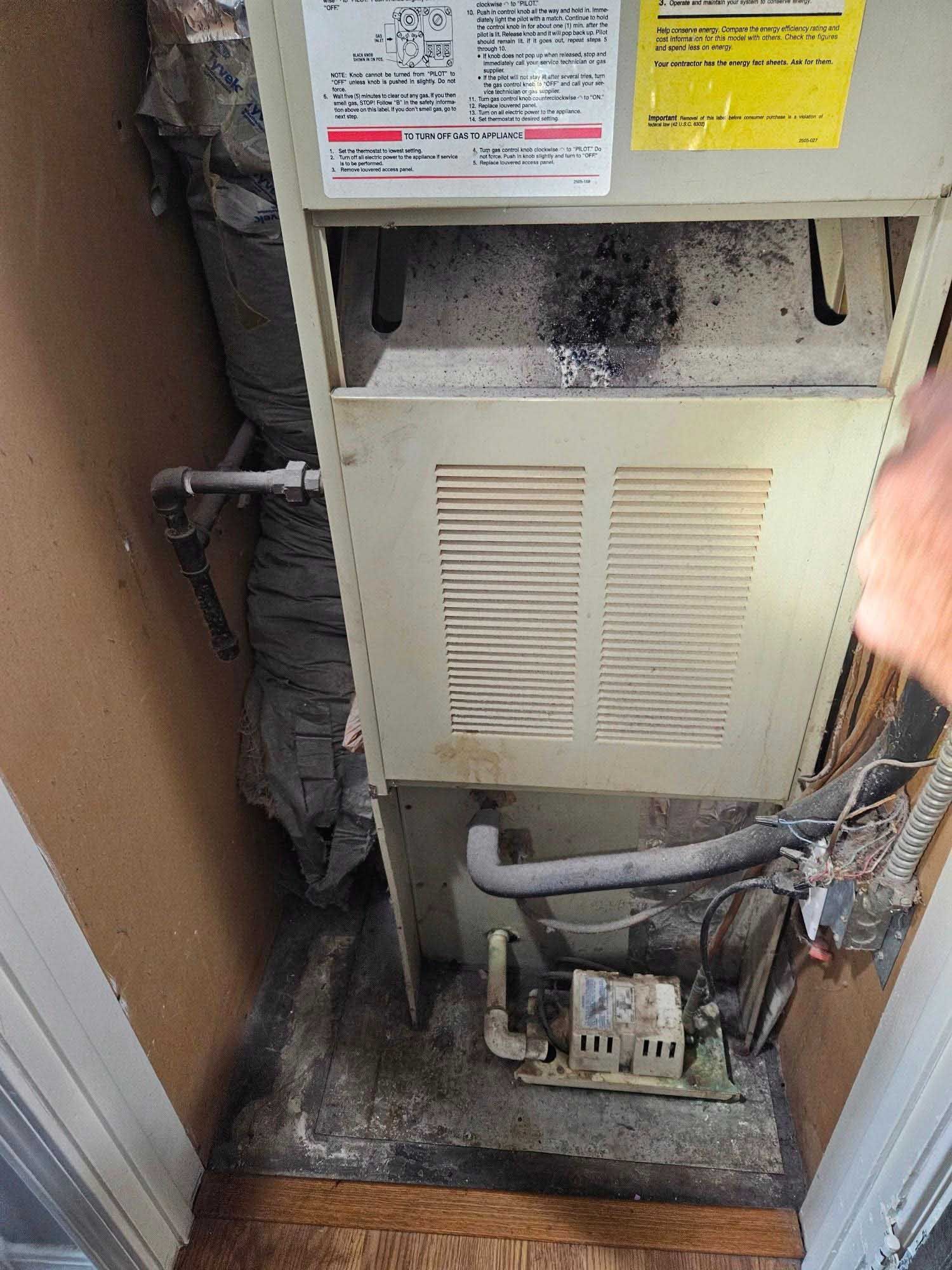 Furnace with a dirty interior and ductwork in a small room.