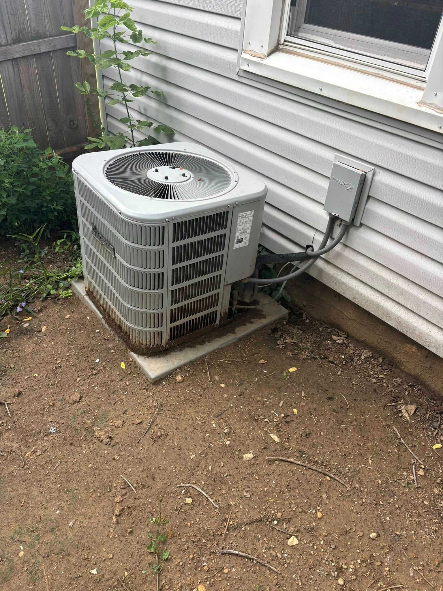 Air conditioner unit outside a house on a concrete pad. Electrical box on the wall.