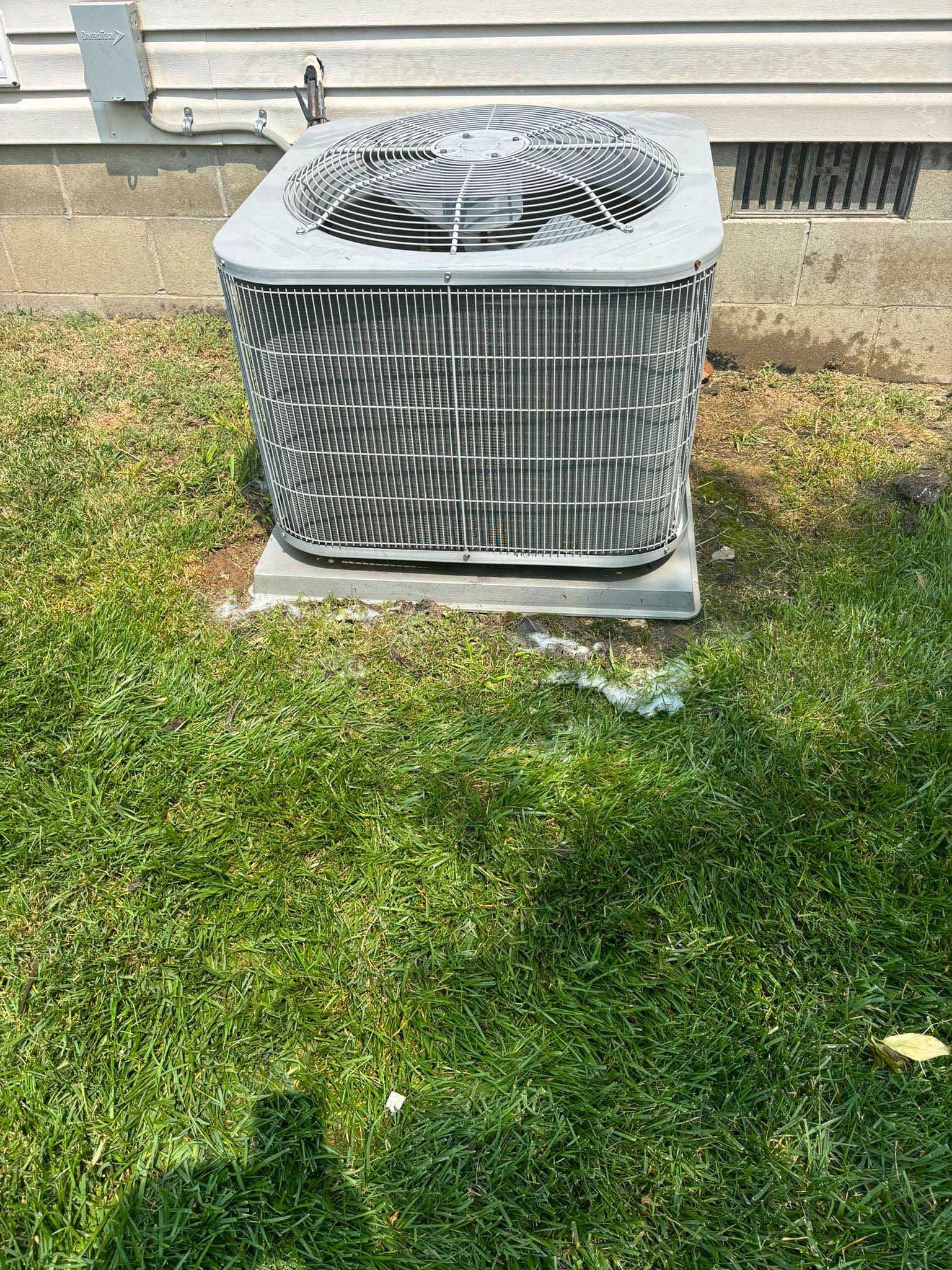 Outdoor air conditioning unit on a concrete pad, surrounded by grass.