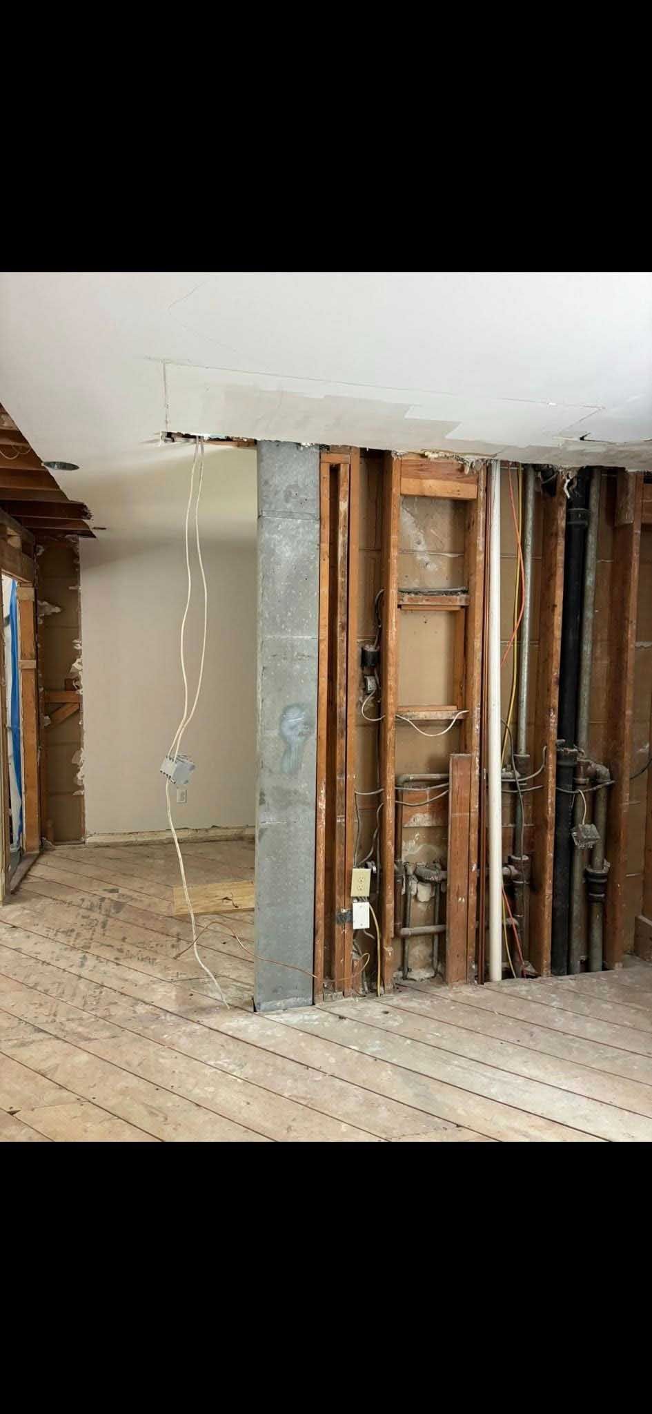 Interior of a building under renovation, showing exposed studs and a central support column.