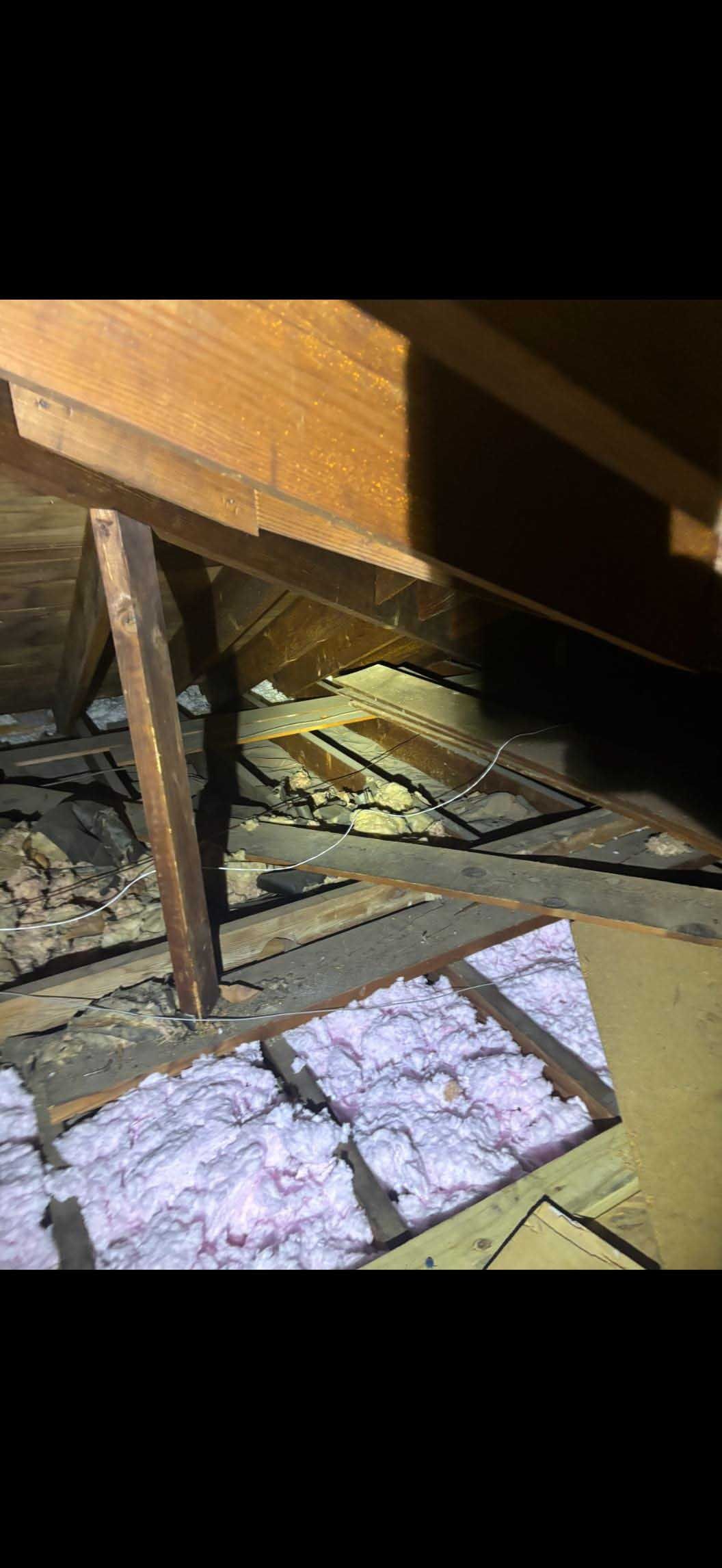 Inside an attic, showing wooden beams, insulation, and a dark, dusty space.