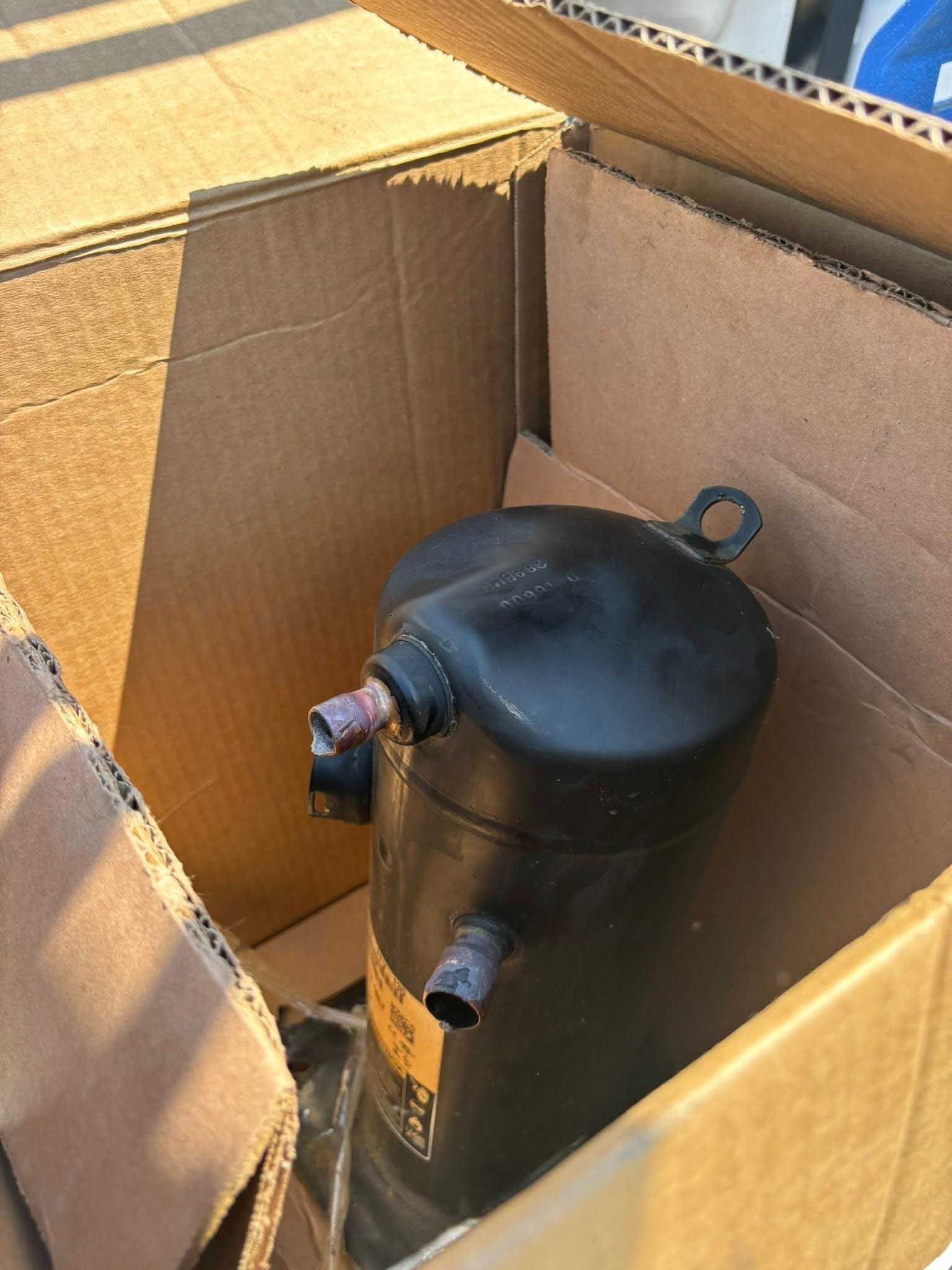 Black HVAC compressor inside a cardboard box.