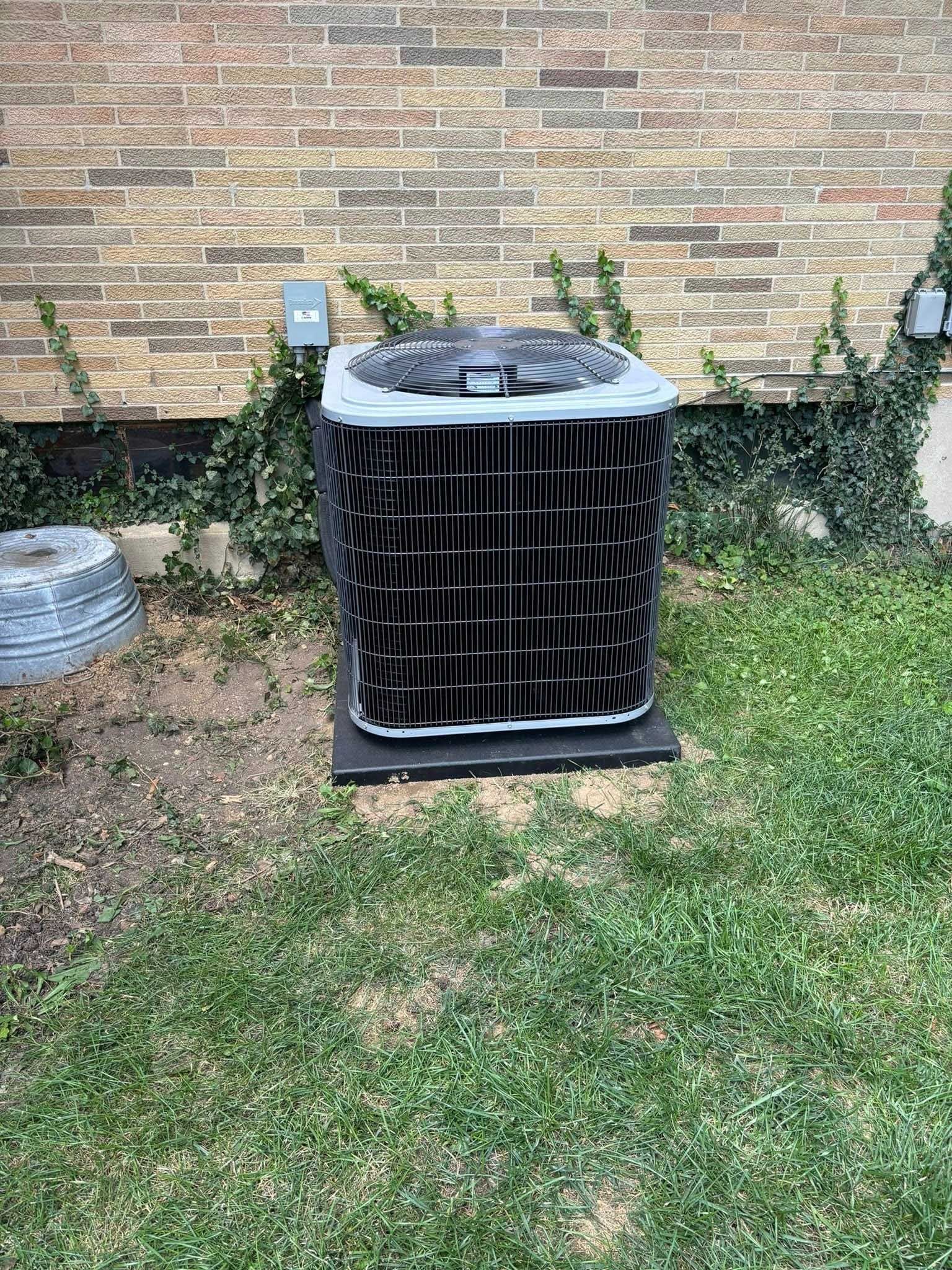 Air conditioning unit on a dark base next to a brick wall with ivy.