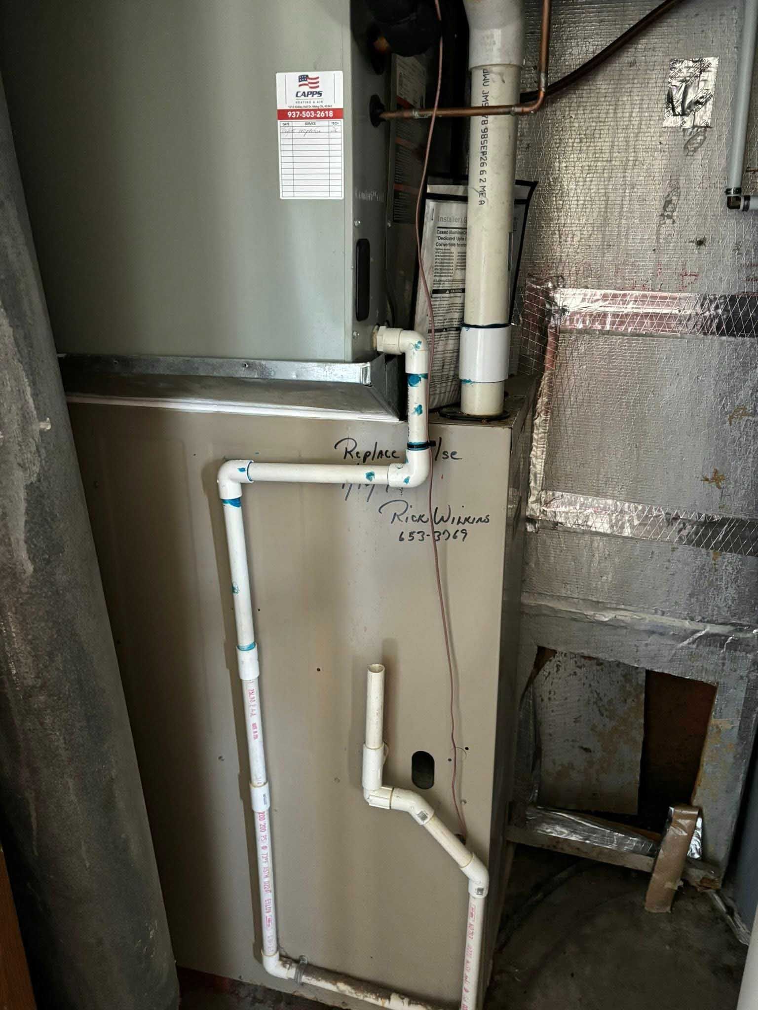 HVAC unit with white PVC drain pipes in a utility space.