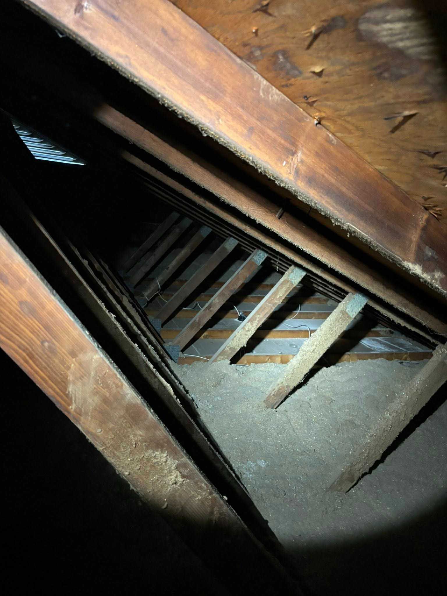Looking up into a dark attic; wooden beams and rafters; dust and debris.