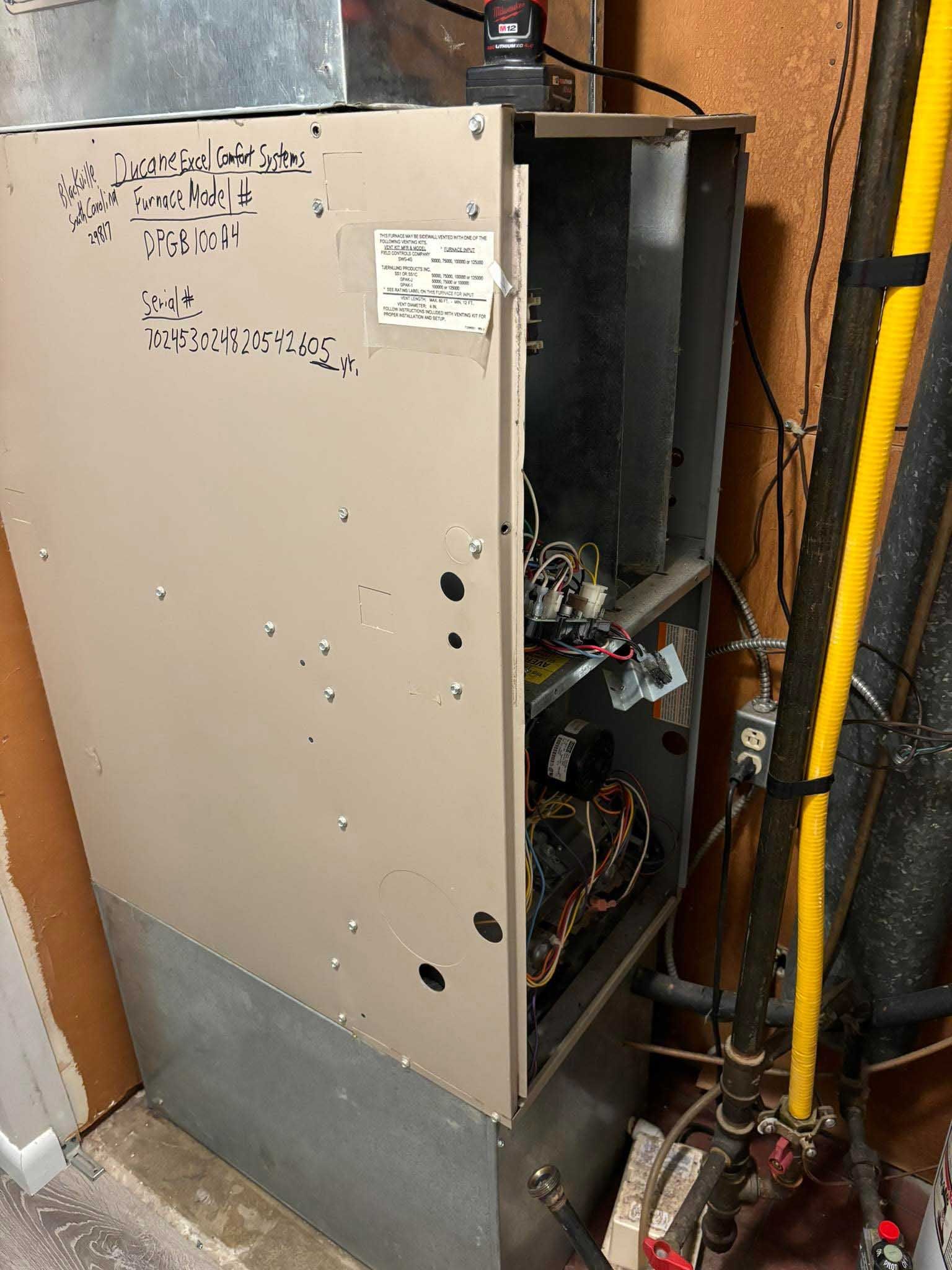 Tan furnace in a basement setting. The unit's panel is open, revealing internal components and wiring.