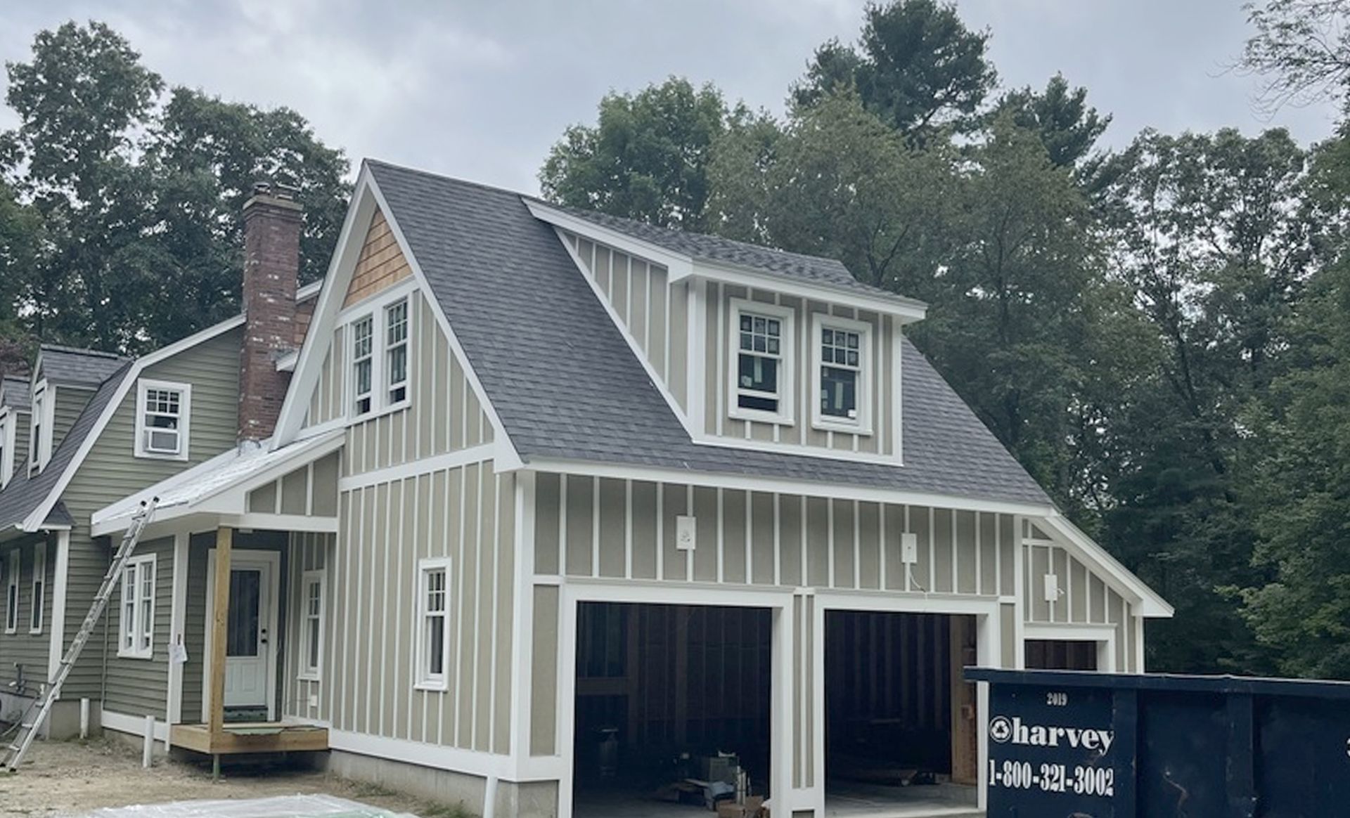 A house under construction with a garage and a dumpster in front of it.