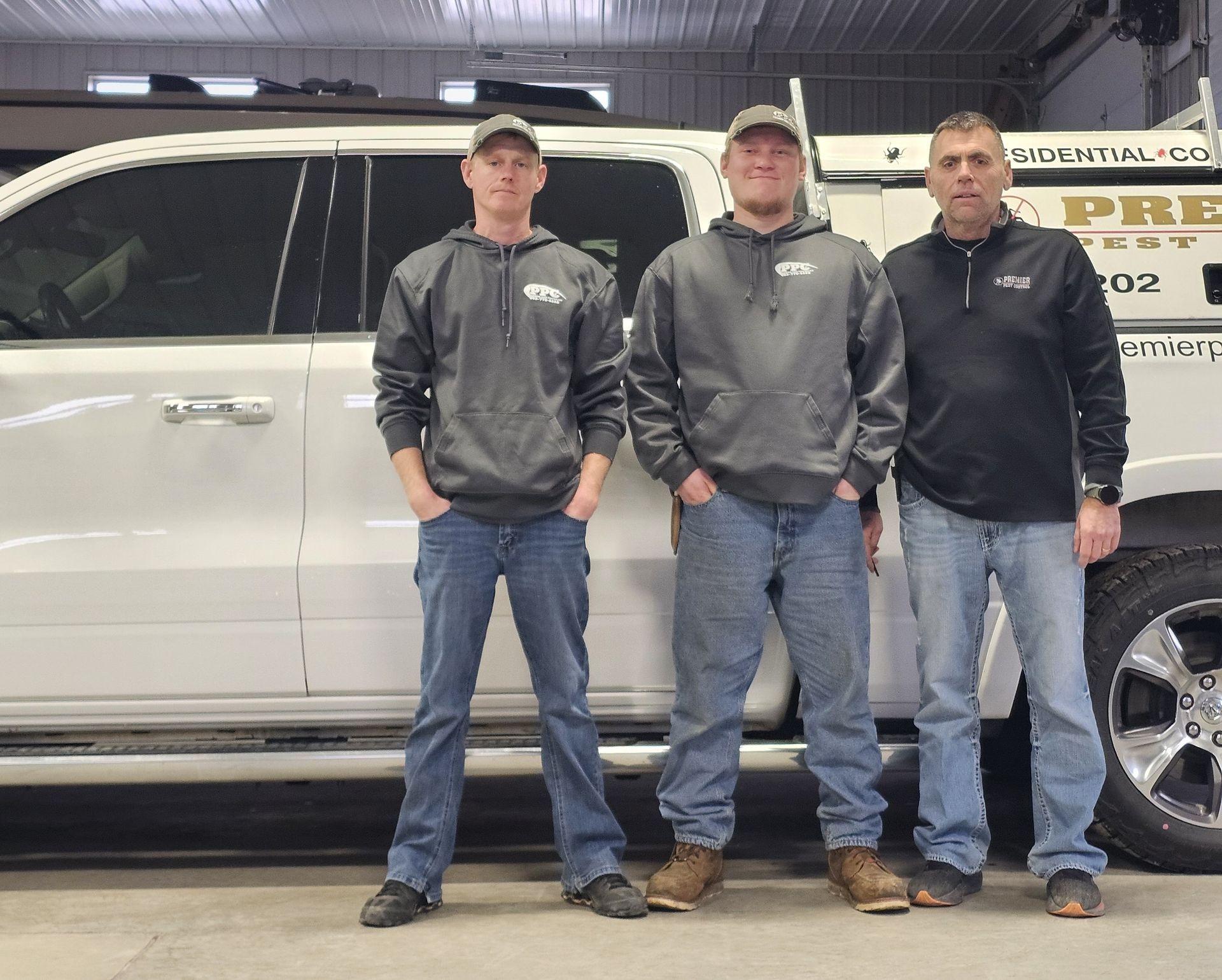 Three people in casual work attire standing in front of a white pickup truck inside a garage.