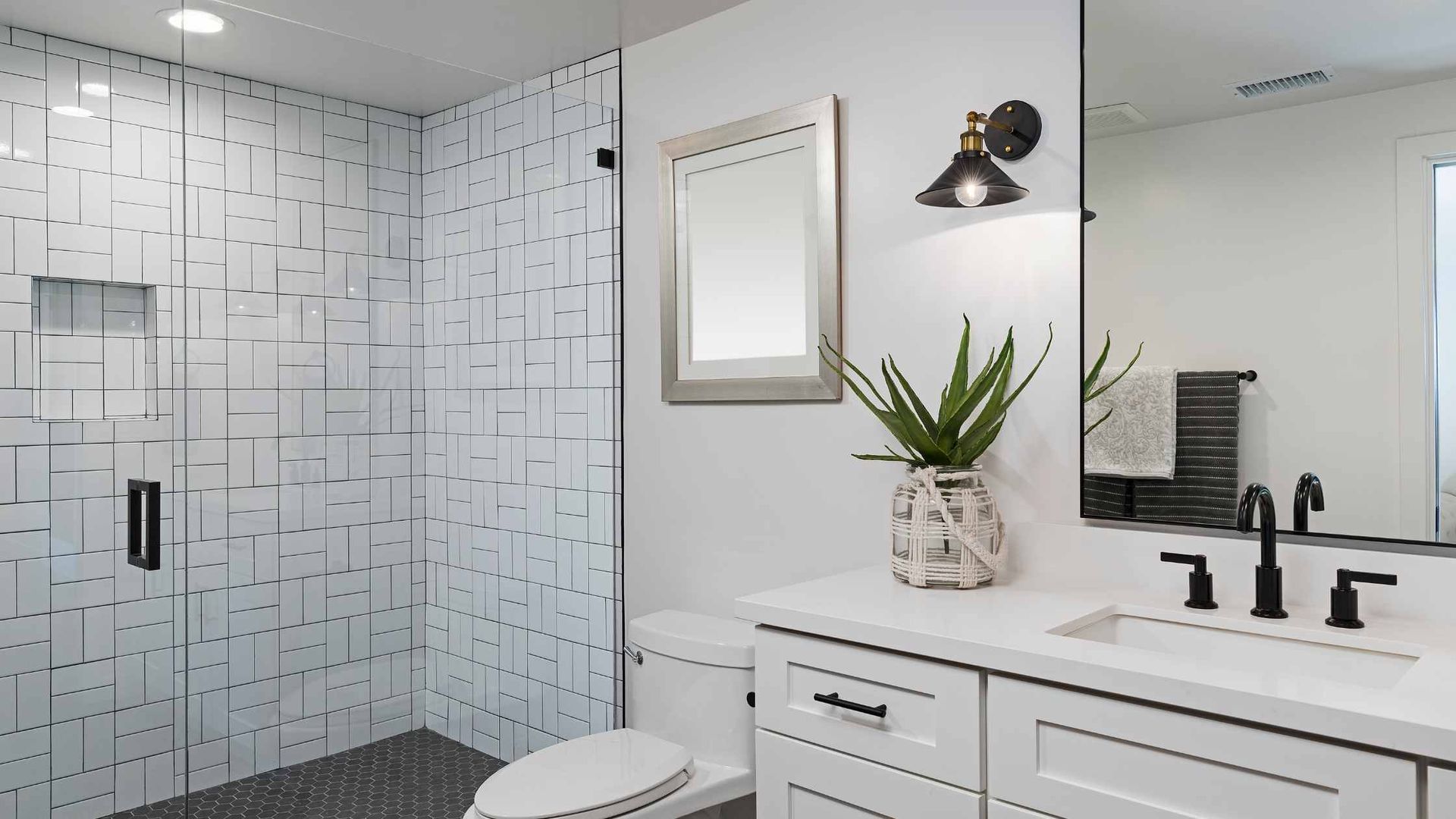 Modern white bathroom with patterned shower, vanity, toilet, and a silver-framed mirror.