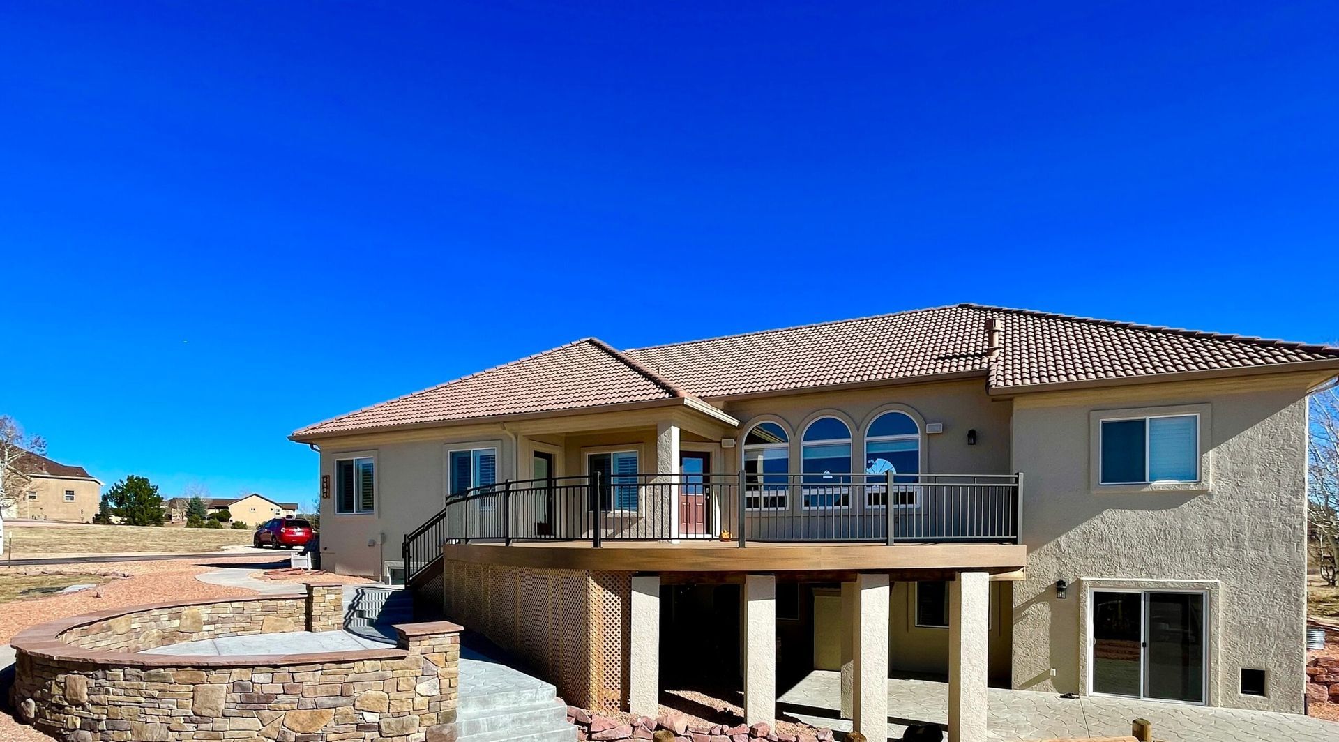 Beige two-story house with a balcony and deck under a clear blue sky.
