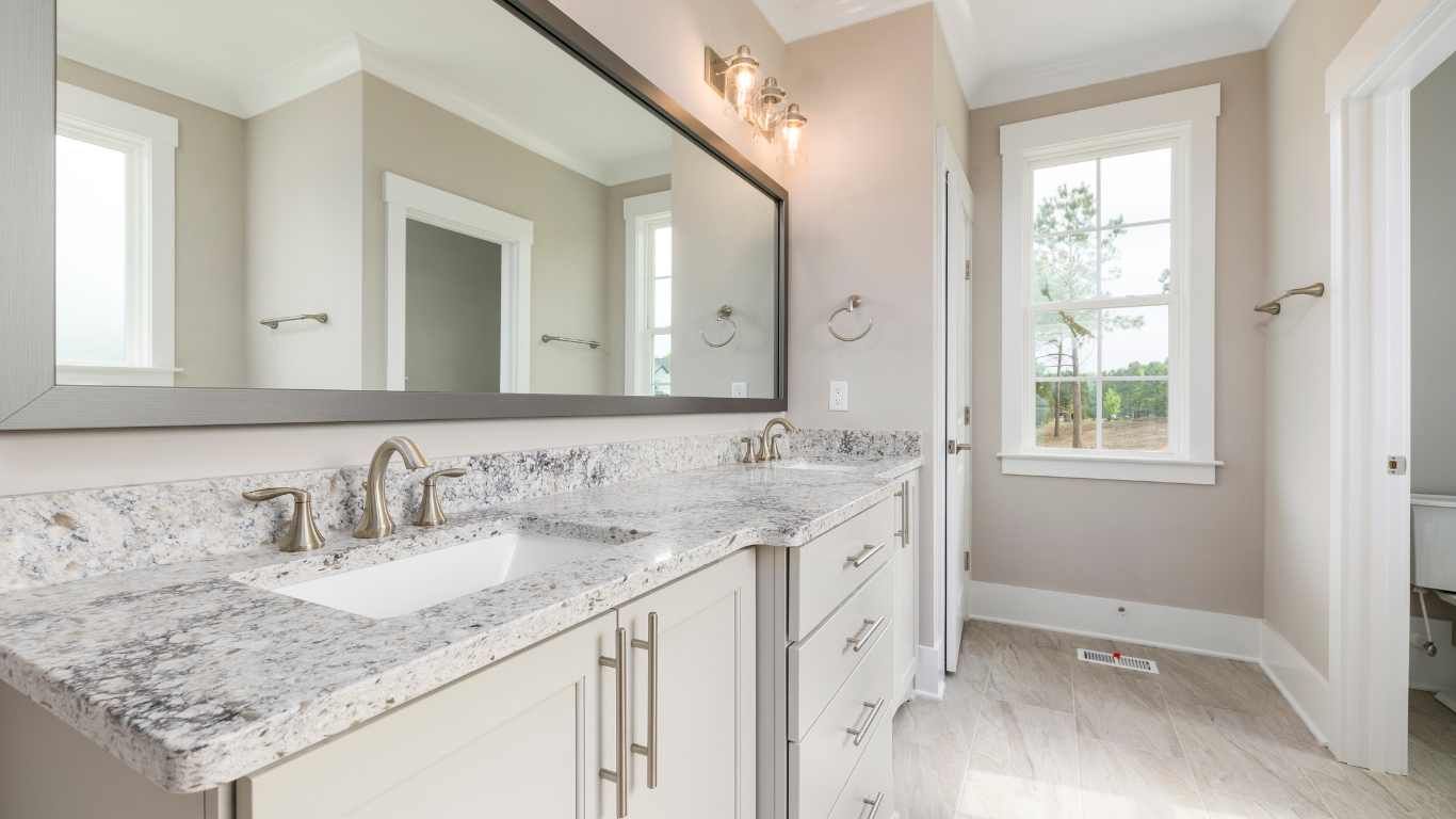 Bathroom with a light-colored countertop, double sinks, a large mirror, and a window.