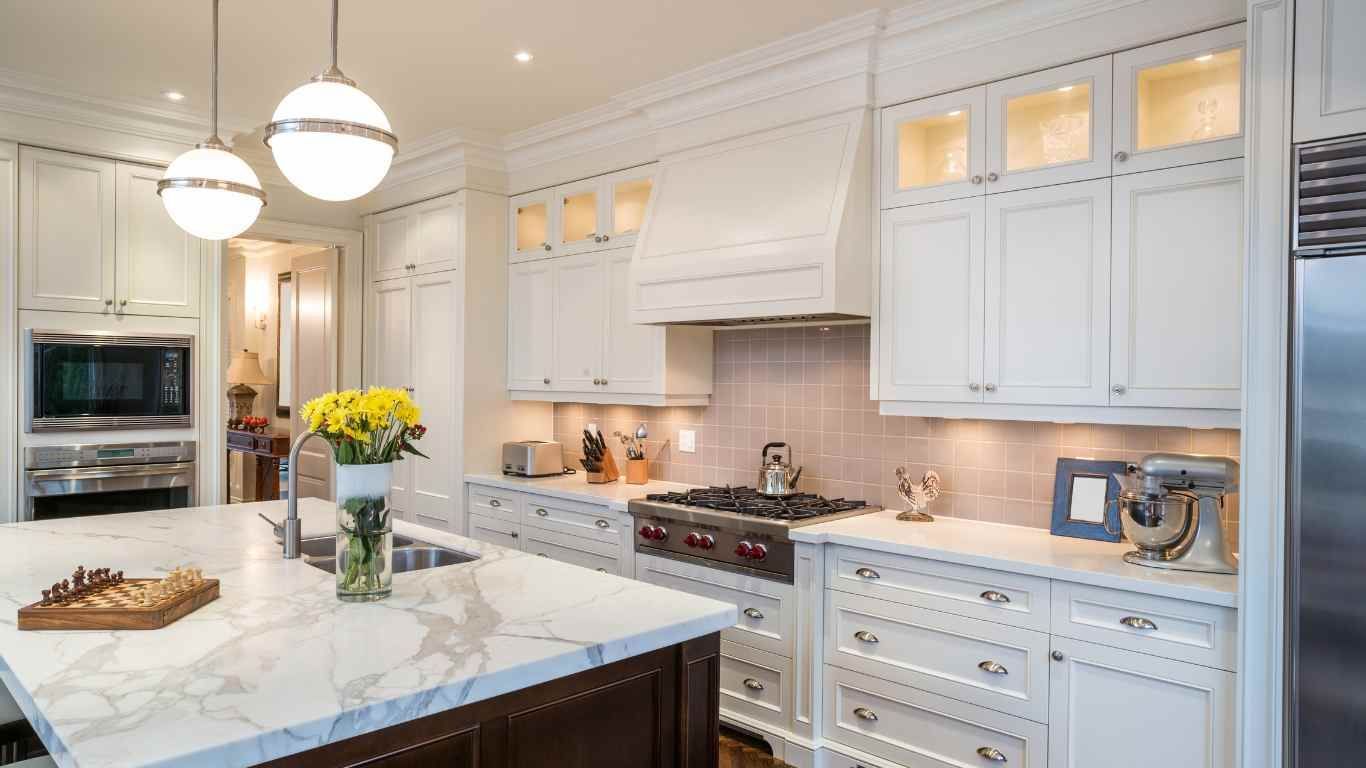 White kitchen with marble island, cabinets, and appliances. Overhead globe lights.