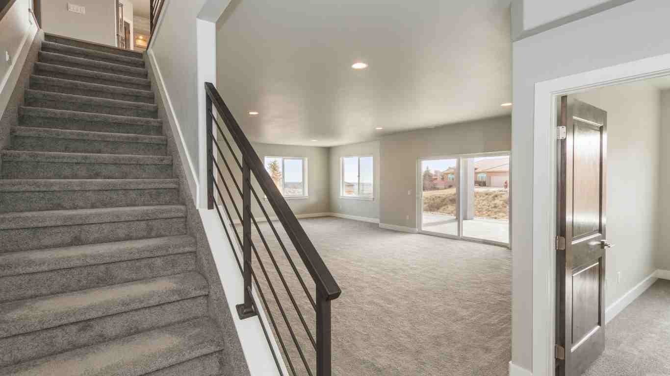 Staircase with gray carpet leads to a curved wall with windows and a door in a house.