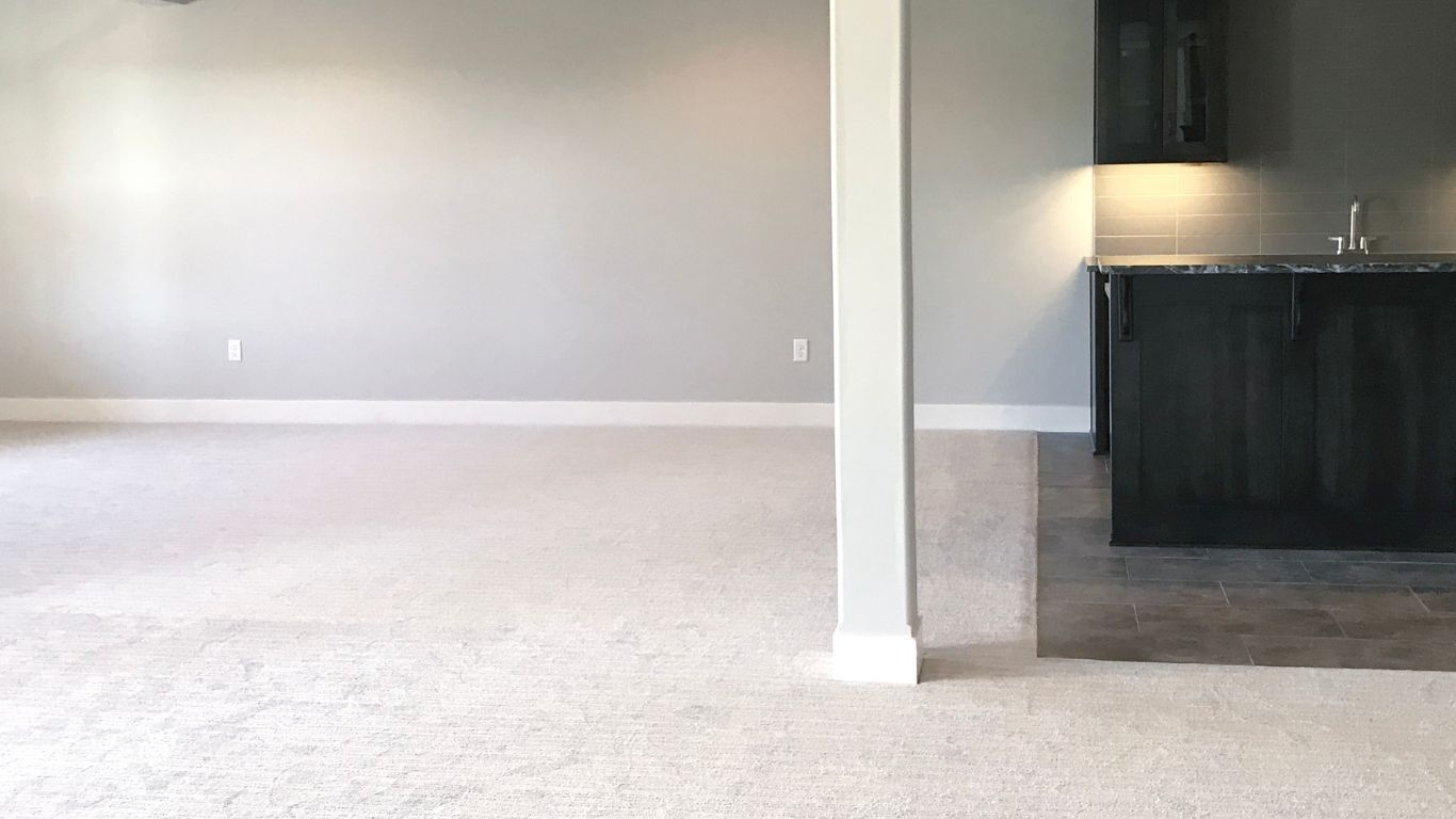 Empty room with gray walls, white carpet, and a dark wood bar.