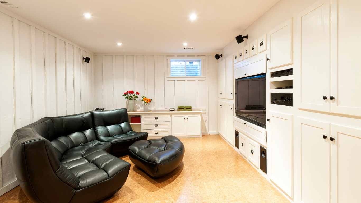 Living room with black leather sectional, built-in white cabinets, cork flooring, and a mounted TV.