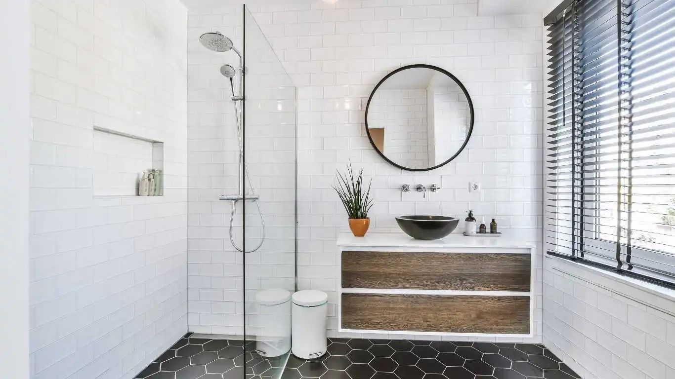 Modern bathroom with black hexagon floor, white tiled walls, glass shower, and wood vanity.