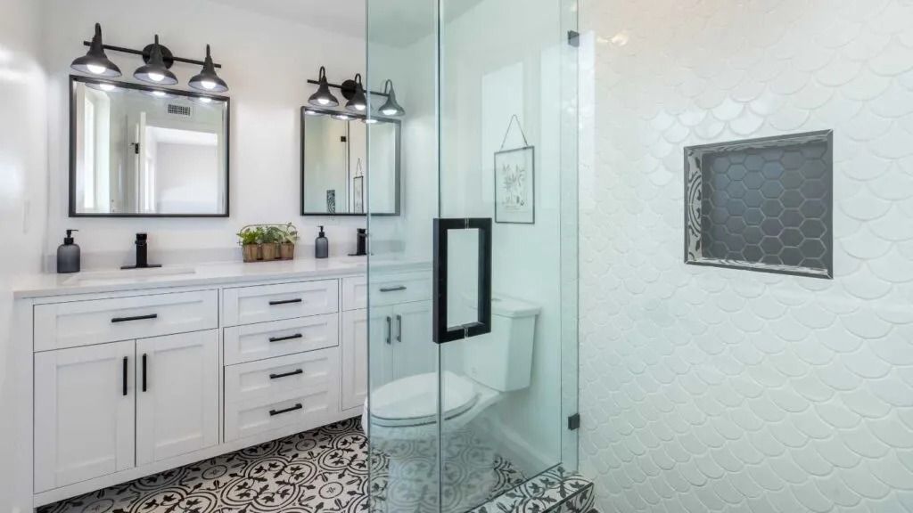 Bathroom with white vanity, black hardware, black and white patterned tile floor, glass shower, and white tile wall.