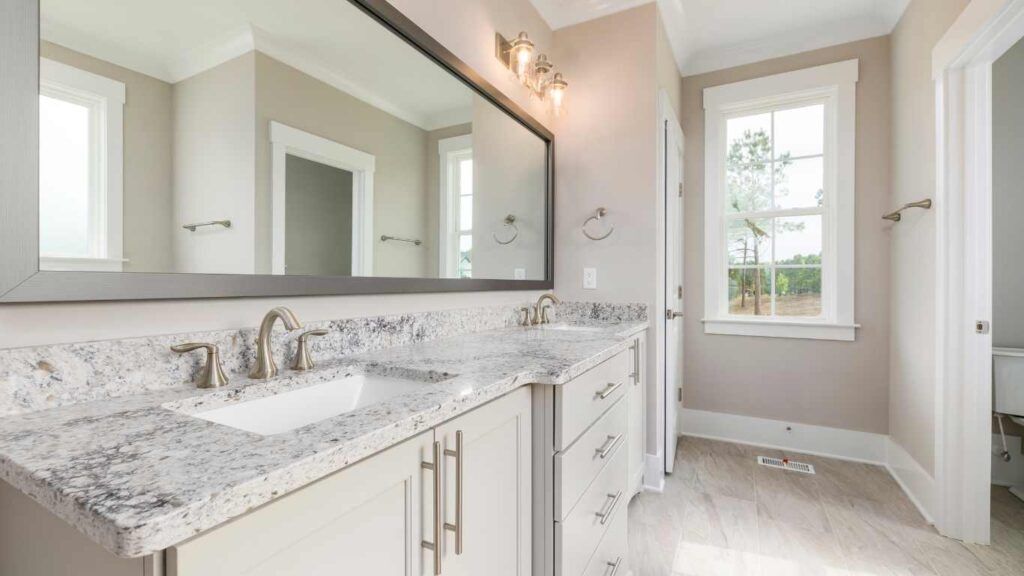 Bathroom with double vanity, large mirror, granite countertop, neutral colors, and window.