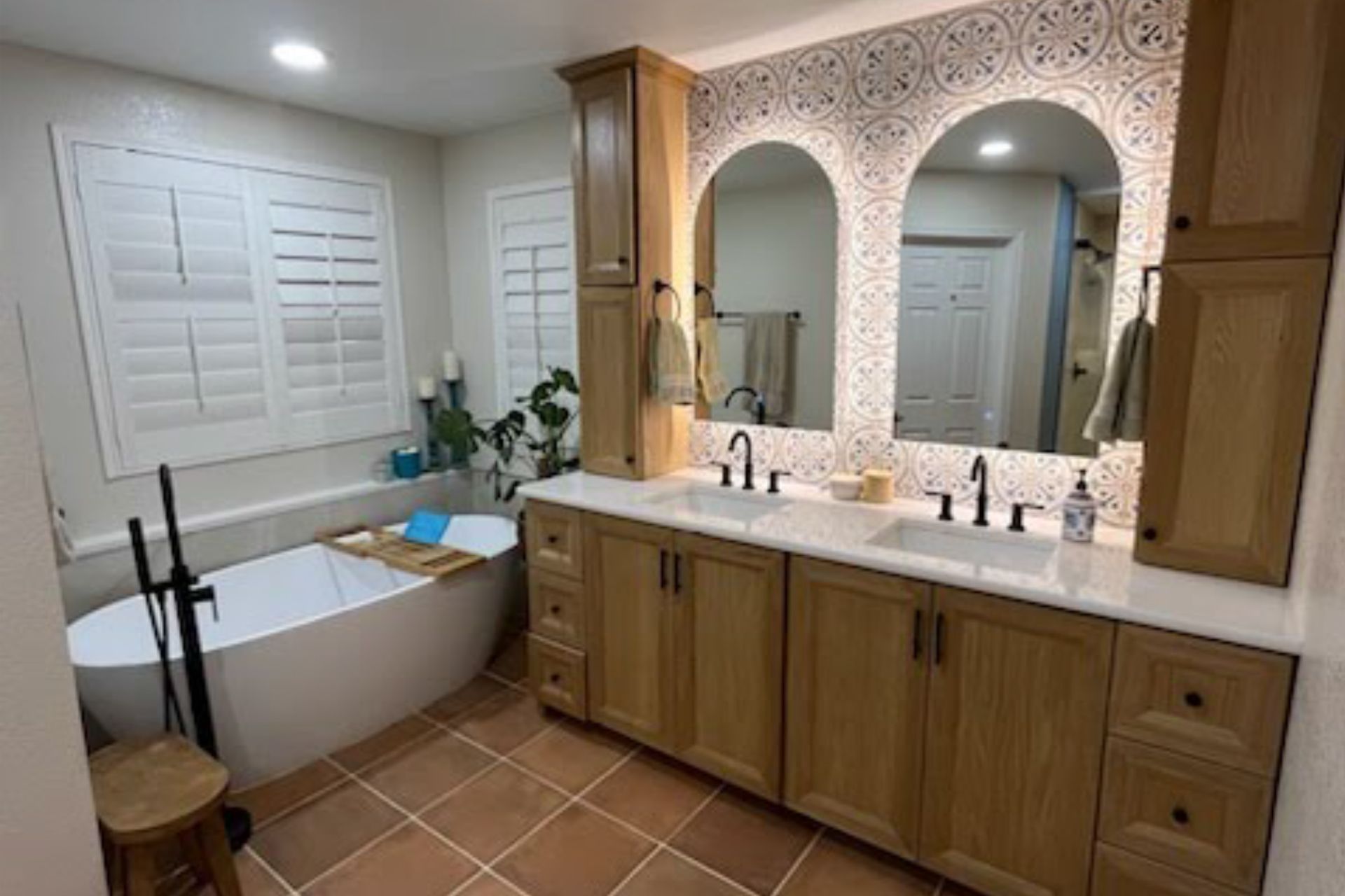 Modern bathroom with a light-wood double vanity, two arched mirrors, patterned backsplash tile, and a freestanding tub.