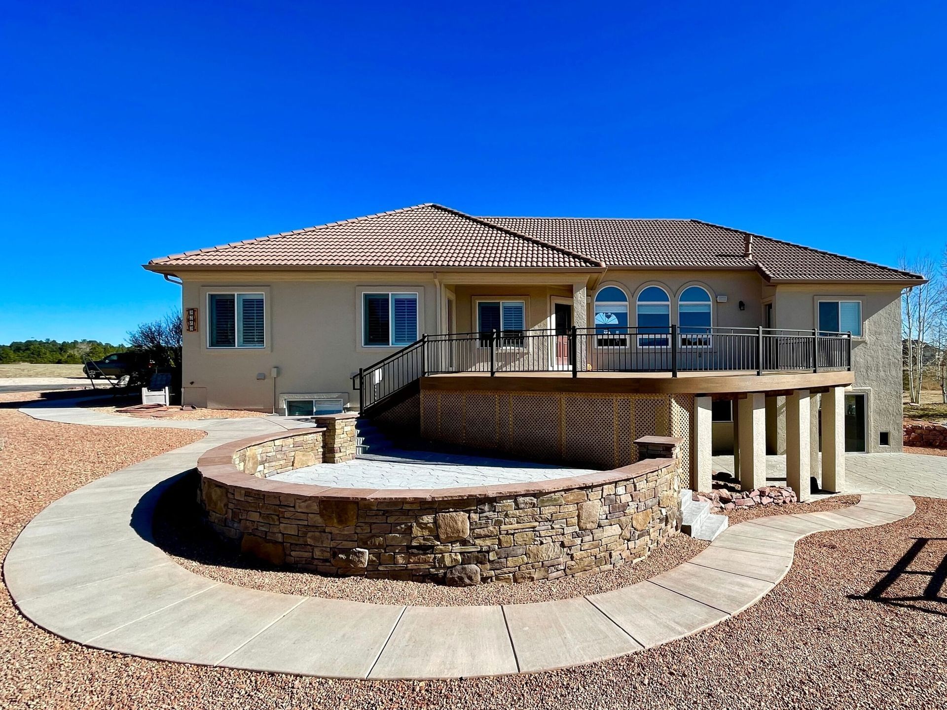 Beige house with a deck and stone patio against a blue sky.