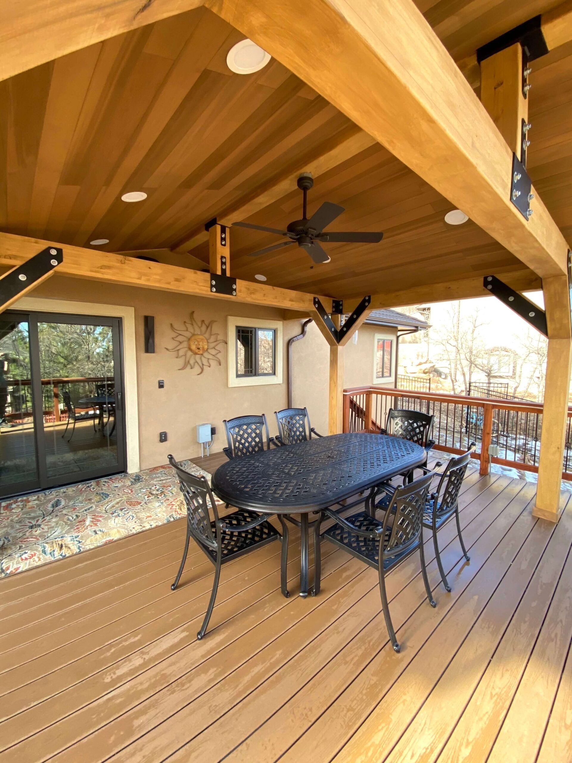 Covered outdoor patio with a dining table and chairs, brown wood deck, and a ceiling fan.